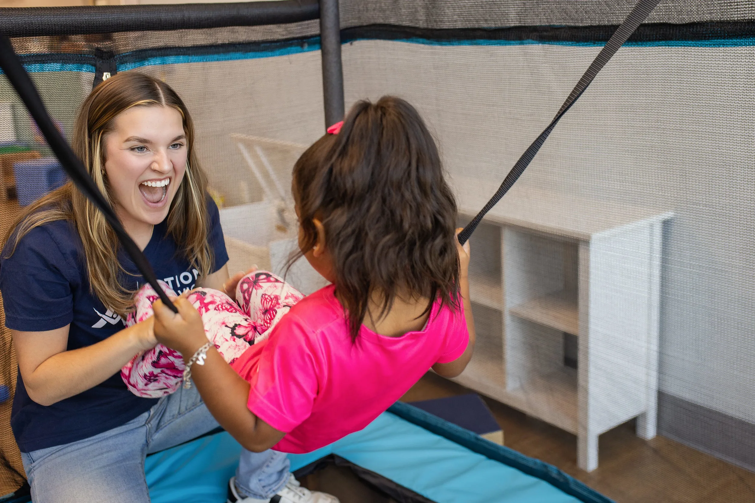 Therapist encouraging a young girl on an indoor swing during an ABA therapy session at Action Behavior Centers.
