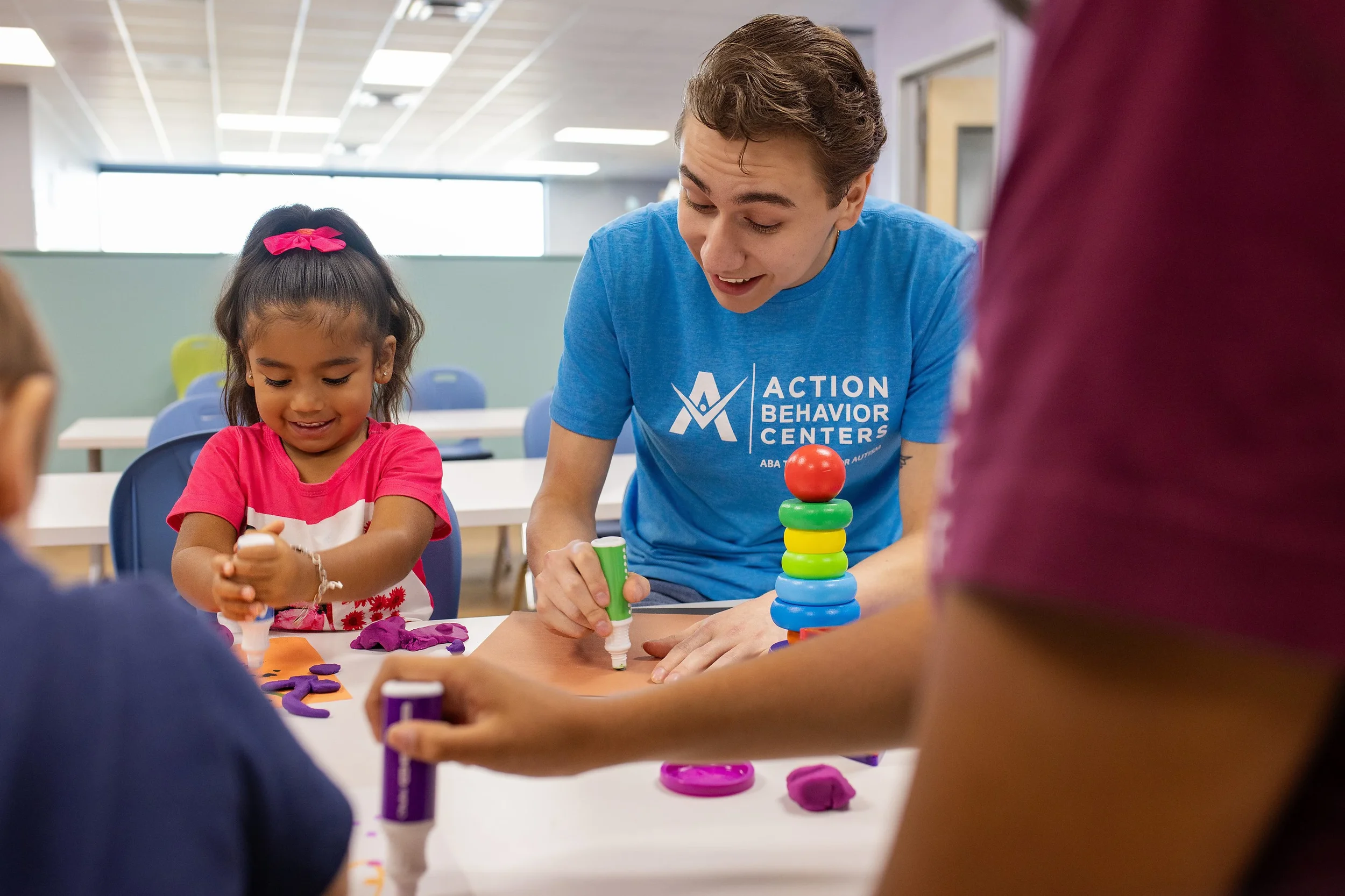 Smiling therapist guides a young girl during an ABA therapy craft session at Action Behavior Centers in San Antonio, Texas.