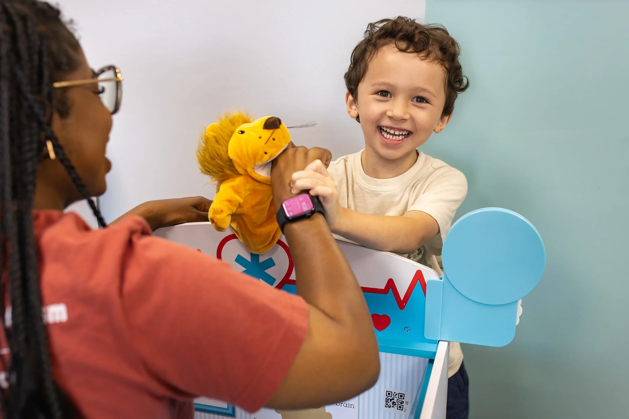 Child laughing and engaging in play therapy with a therapist using a puppet during a social interaction session at Action Behavior Centers in San Antonio.