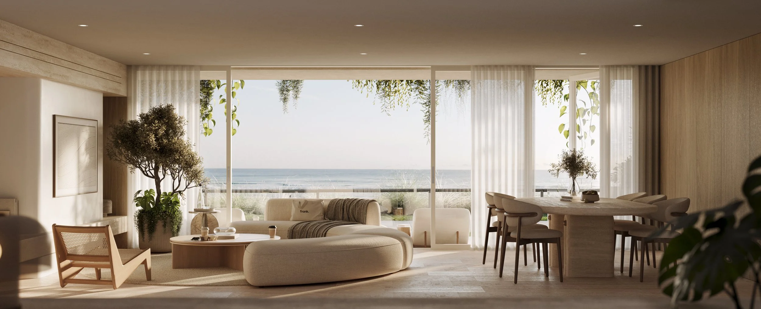 Modern living room with large windows overlooking the beach, featuring neutral-toned furniture, green plants, and natural light.