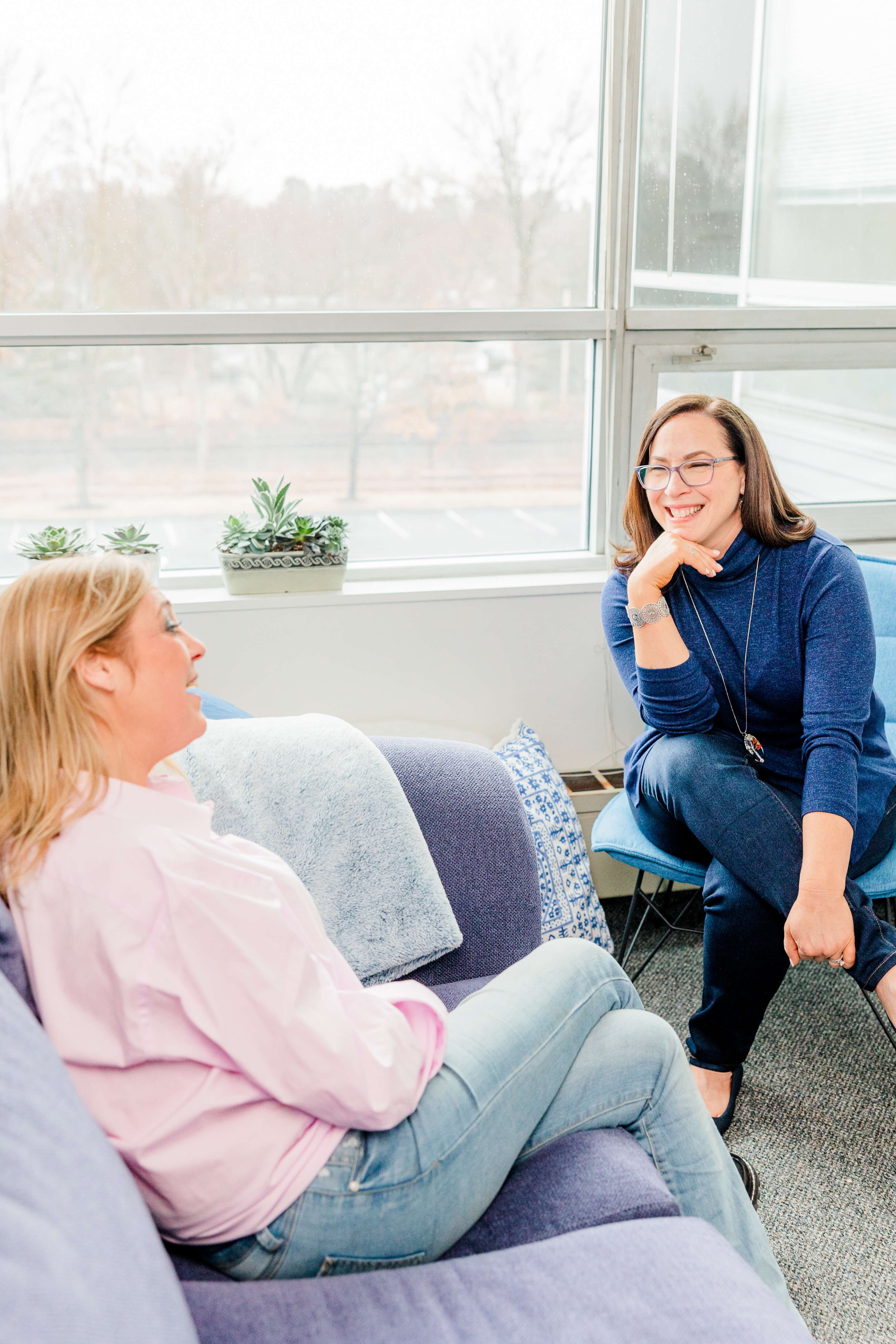 Jill sitting in a chair in her Natick, MA therapy office talking with a client who's sitting on the couch opposite her