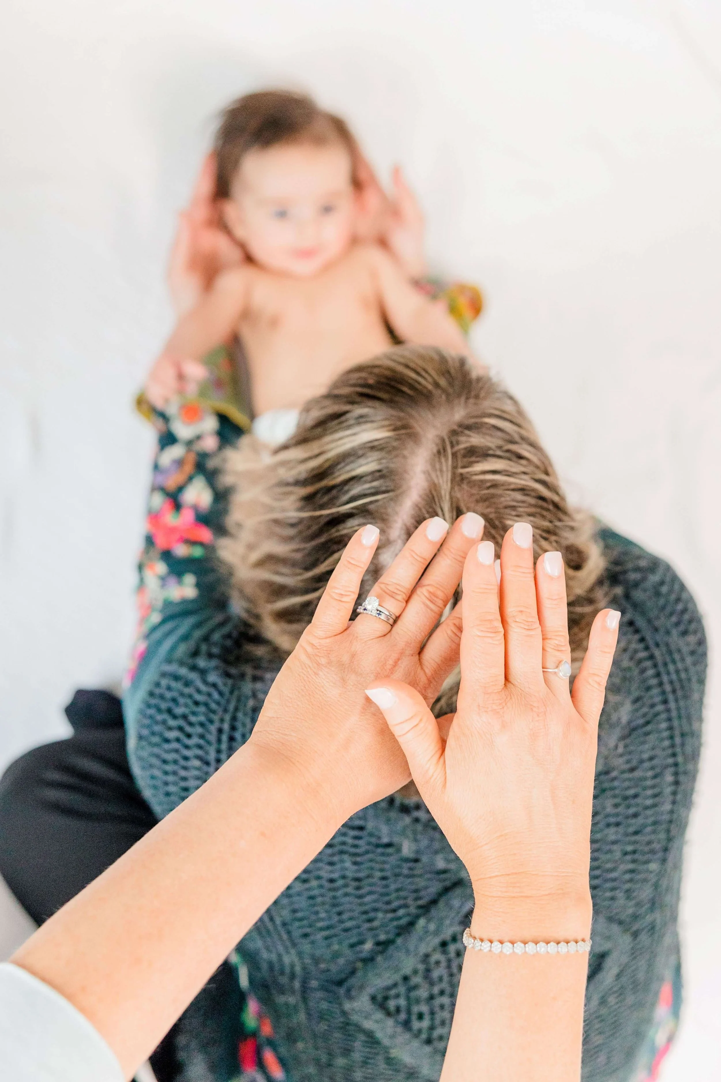 Jill places her hands on a Mom's head while she's holding her baby during an infant reiki massage class