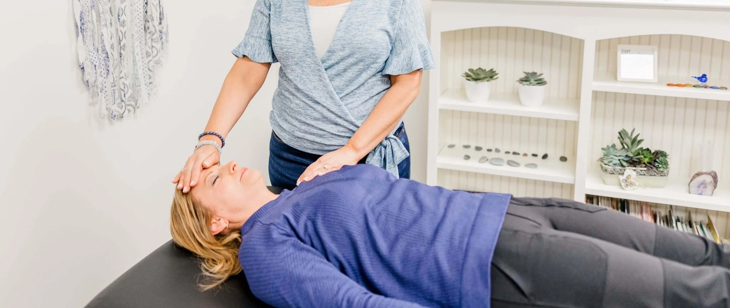 A client is on the table in Jill's Natick, MA Therapy office. Jill's hands are on the client's head and shoulder during a Reiki healing session.