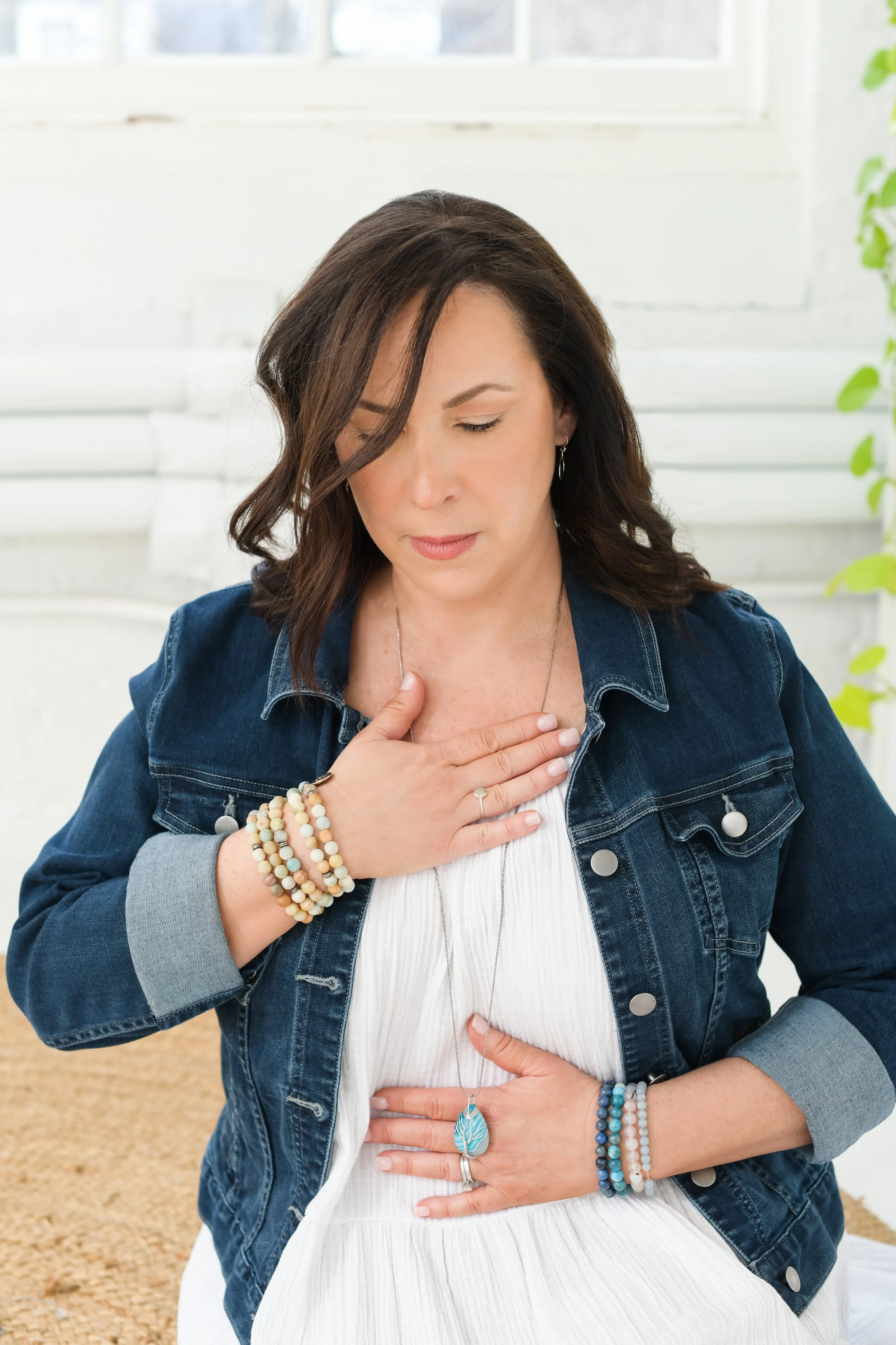 Jill Vetstein, spiritual coach and therapist in her natick, ma office sitting with hands on her heart and sacral chakra and breathing.