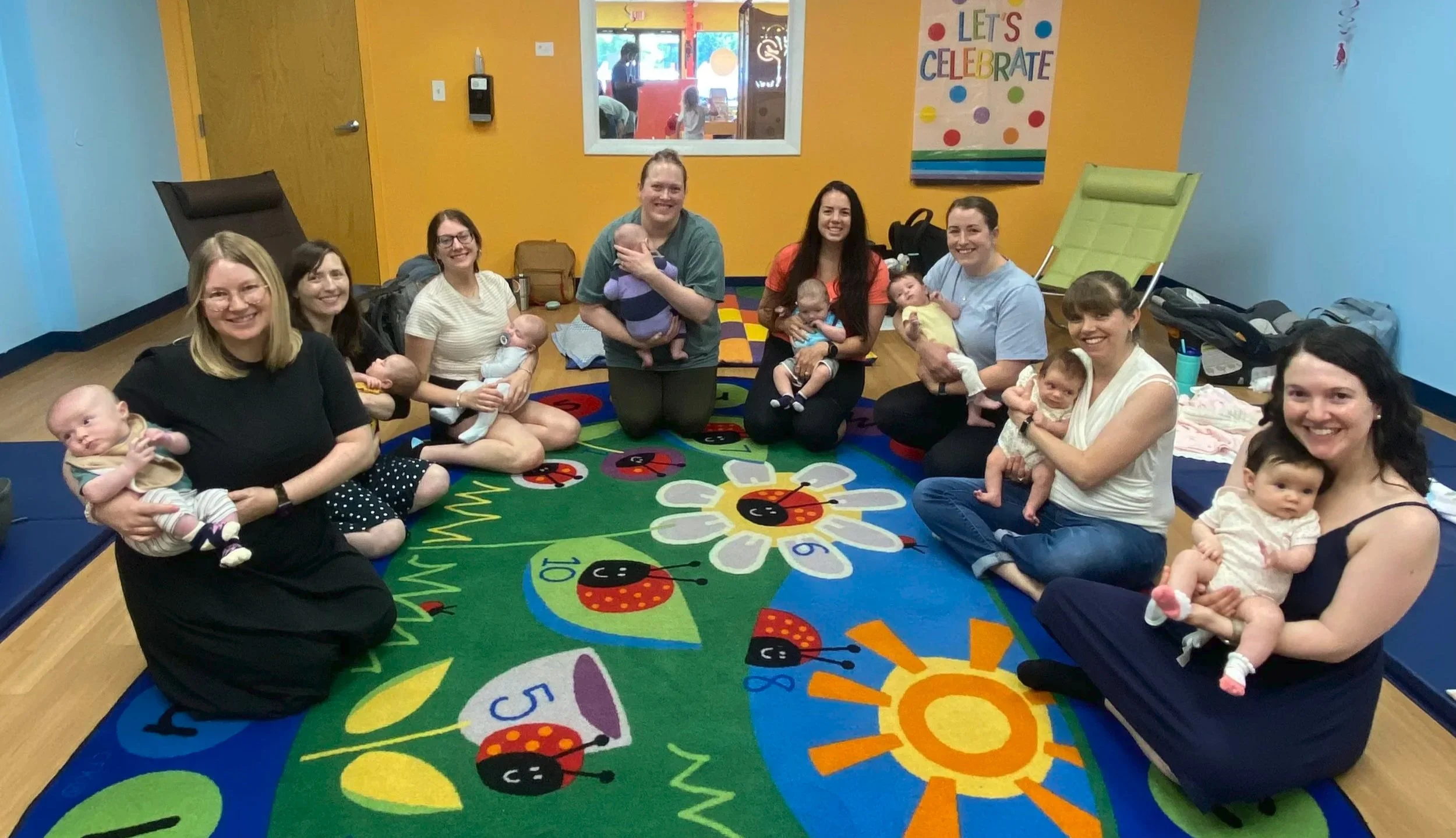 Moms in a classroom sitting on the floor holding their babies in a semi-circle as participants in the Mindful Mom and Baby Group with Jill Vetstein and Jessica Spaman