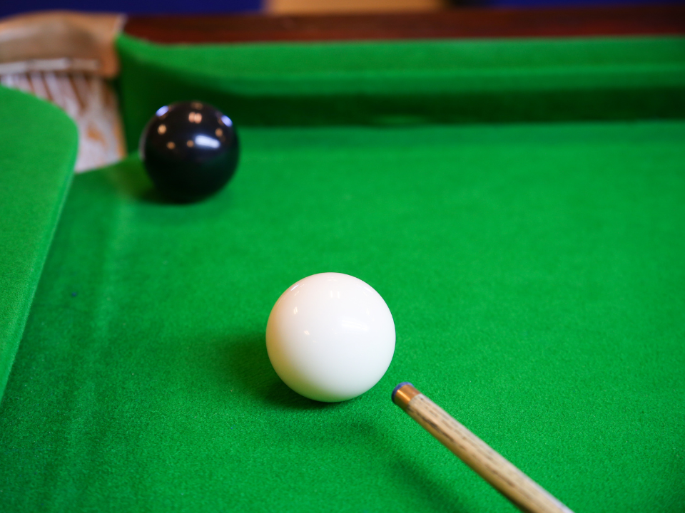 White snooker ball on green cloth pointing towards a black ball in the corner