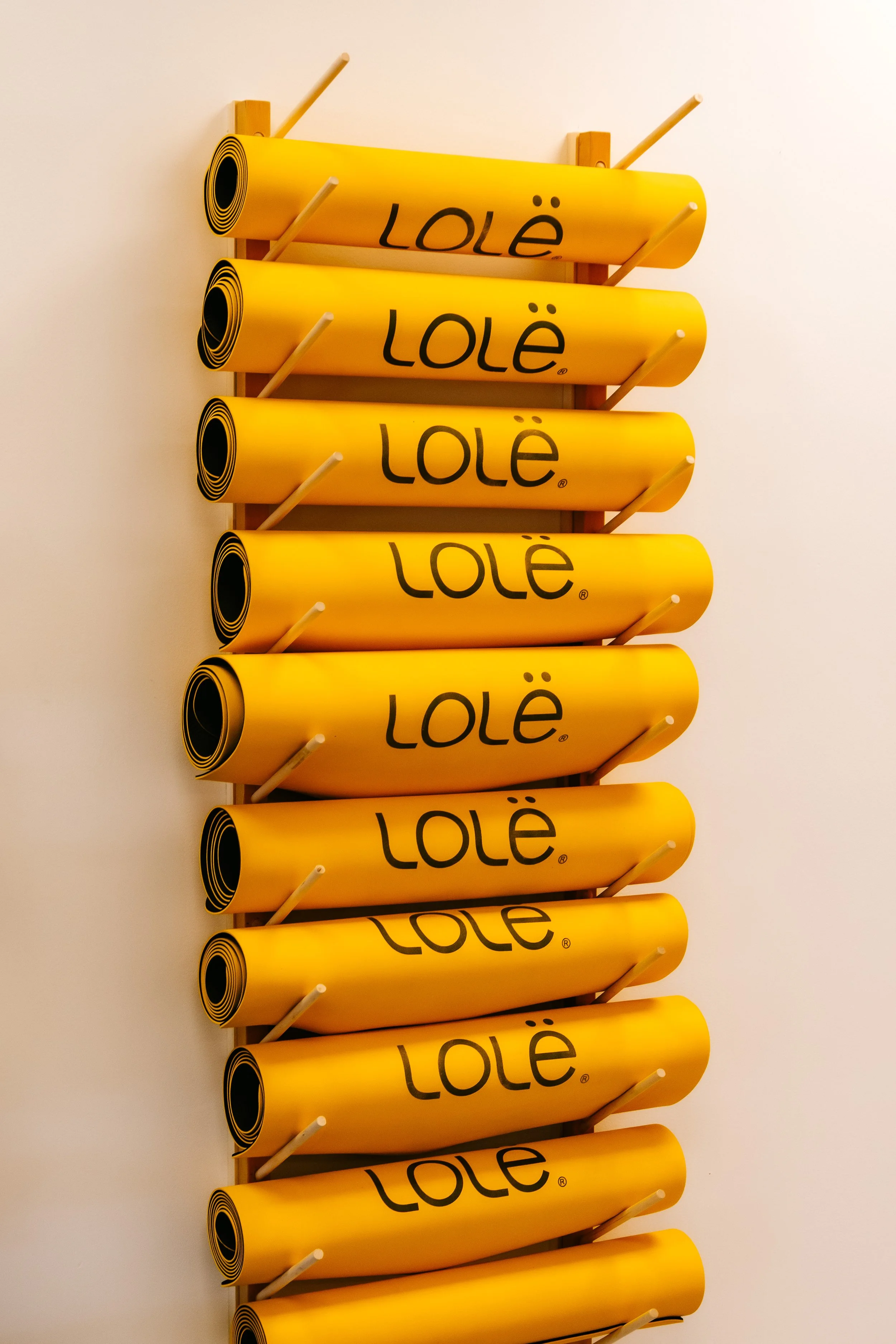 Une sculpture en forme de rouleaux de tapis de yoga jaunes avec le mot 'LOLË' écrit dessus, fixée au mur par des supports en bois.