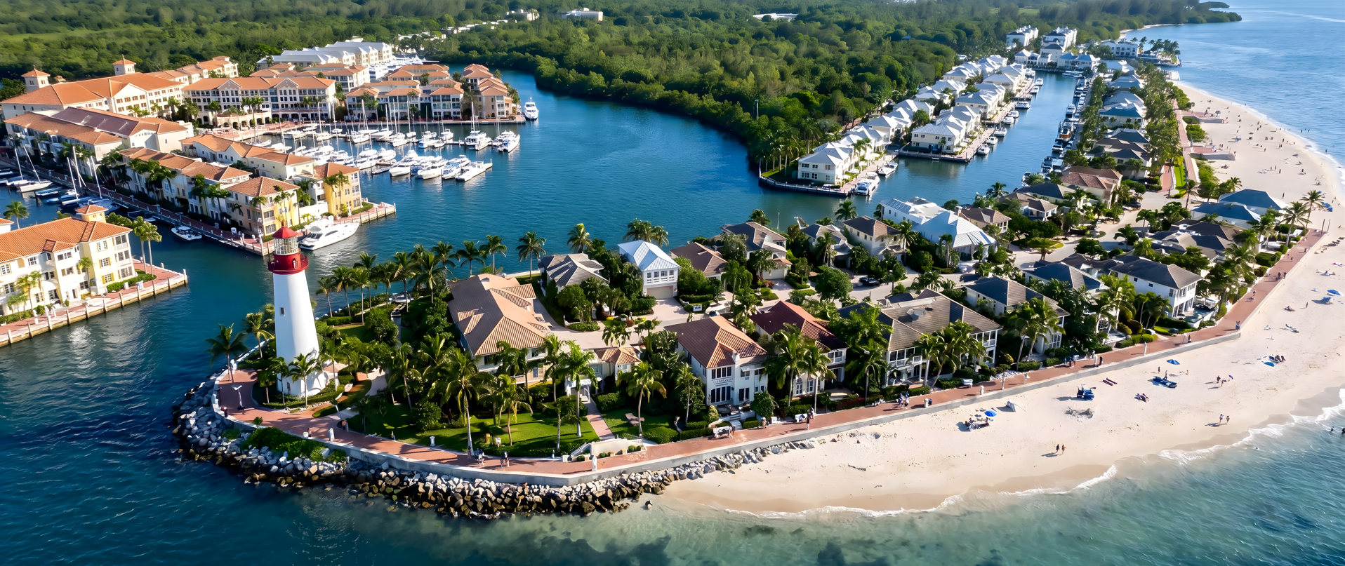 A coastal resort residential town with a lighthouse, houses, a marina with boats, and a sandy beach with people and umbrellas.