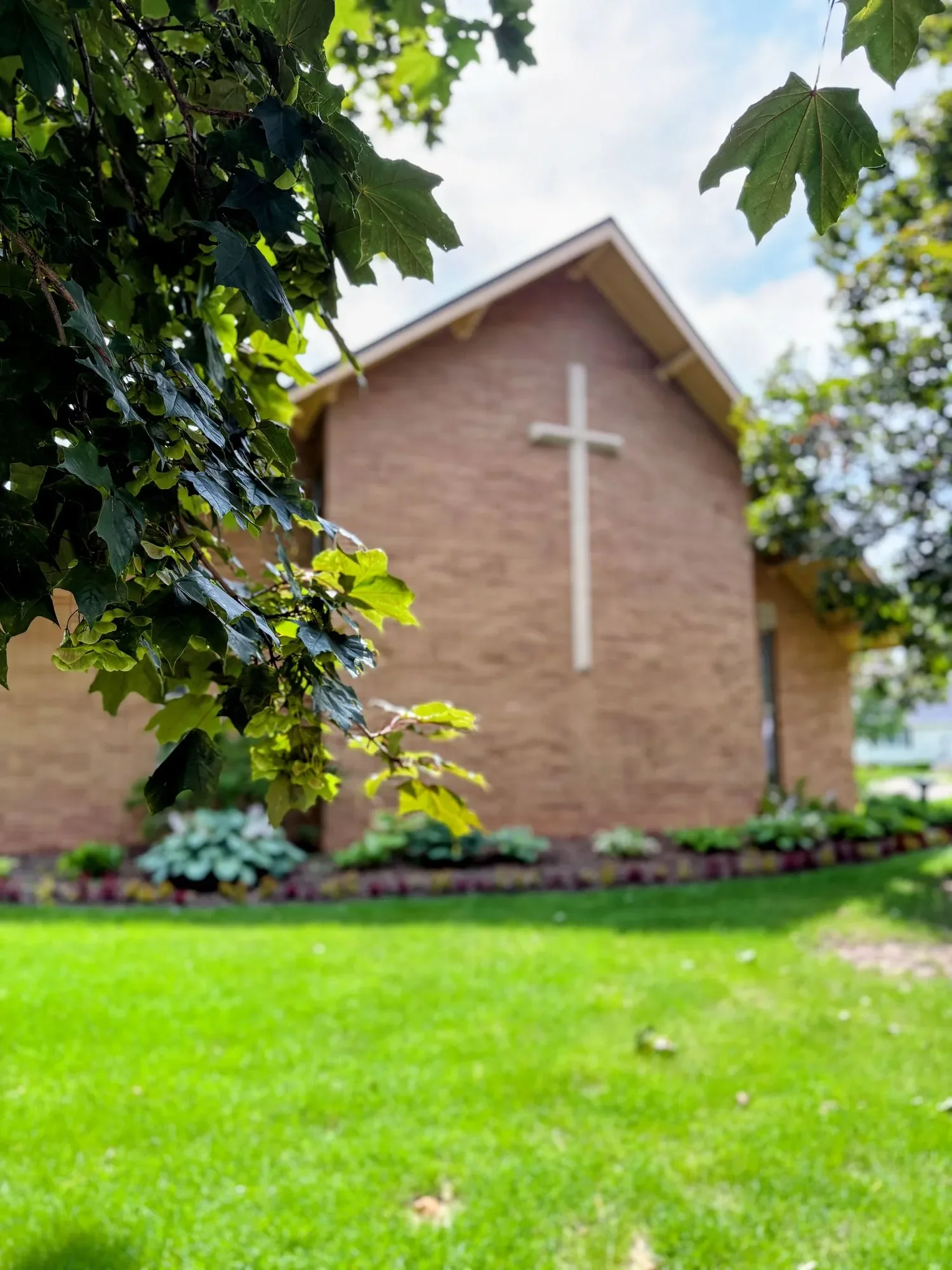 Exterior of Christ Alone Church, an independent Reformed church in Green Bay, Wisconsin, with a tall cross and garden beds along the wall