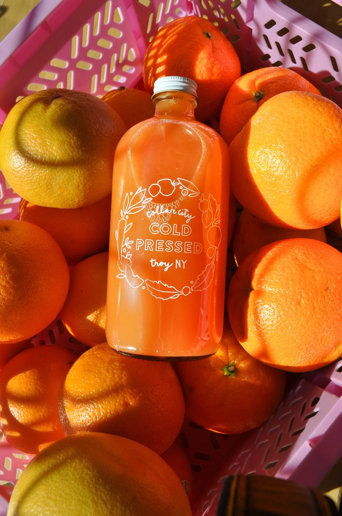 Glass jar of fresh-squeezed orange juice surrounded by whole and sliced oranges, beverage photography for a Troy, NY café