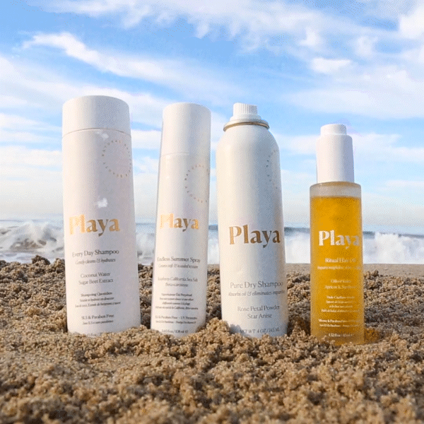 Four Playa haircare products on sandy beach with ocean background