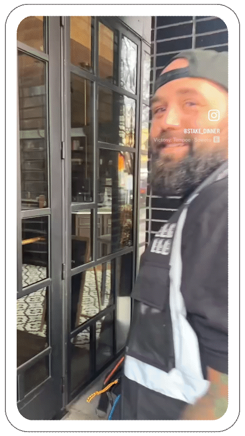 A person with a beard and backward cap, standing in front of a glass door. The interior visible has patterned floor tiles.