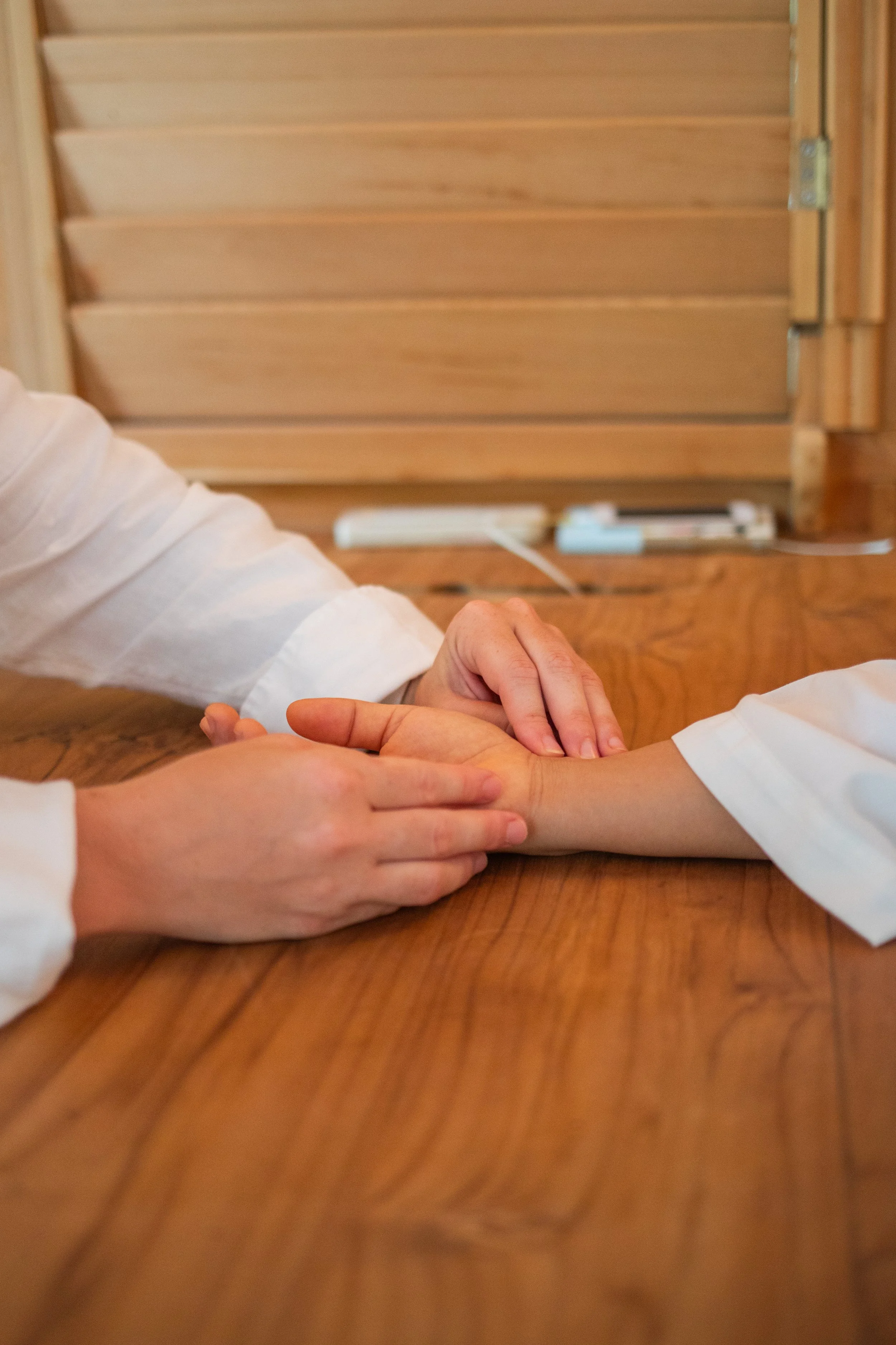 A person holding another person's wrist while checking their pulse at a wooden table.