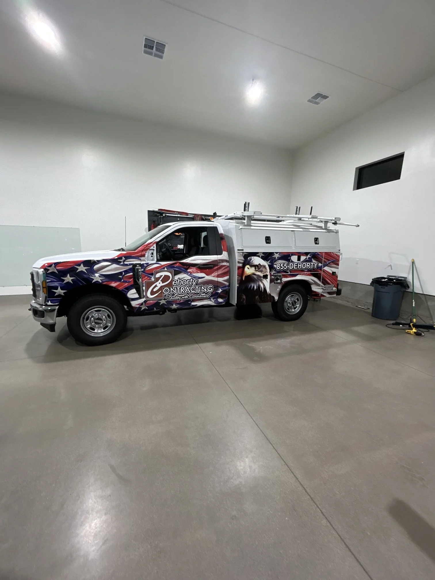 Interior of an empty garage with a utility truck parked inside. The truck has patriotic-themed truck wrap with an eagle and contact information. Full wrap on truck.