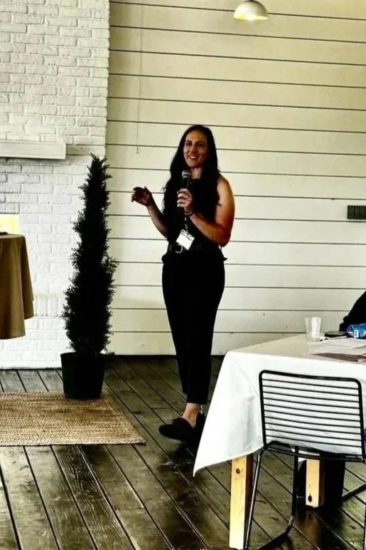 Dr Erin Ayala standing in an event space and speaking in a microphone