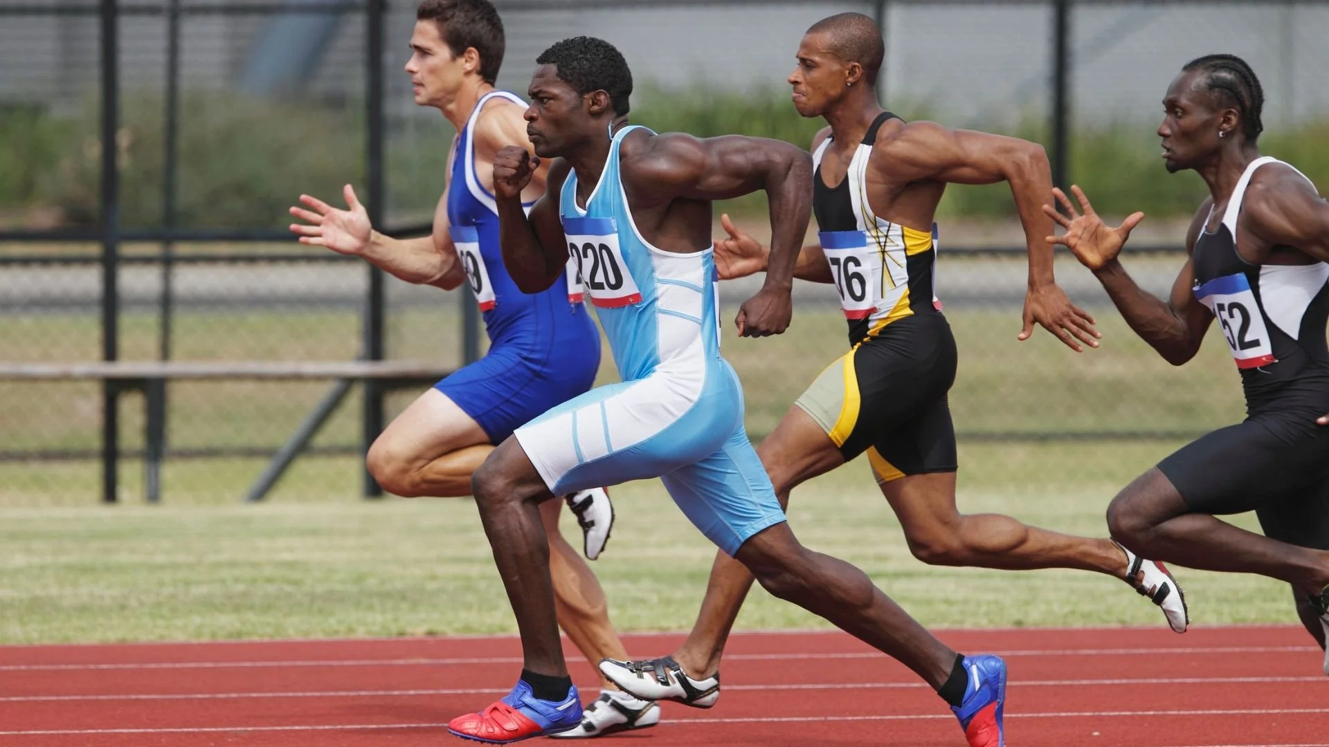 Four sprinters competing in a track and field race on a red running track.