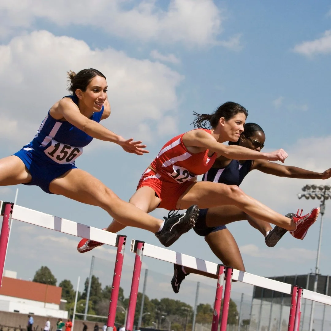 Female track and field athletes jumping over hurdles during a competitive race