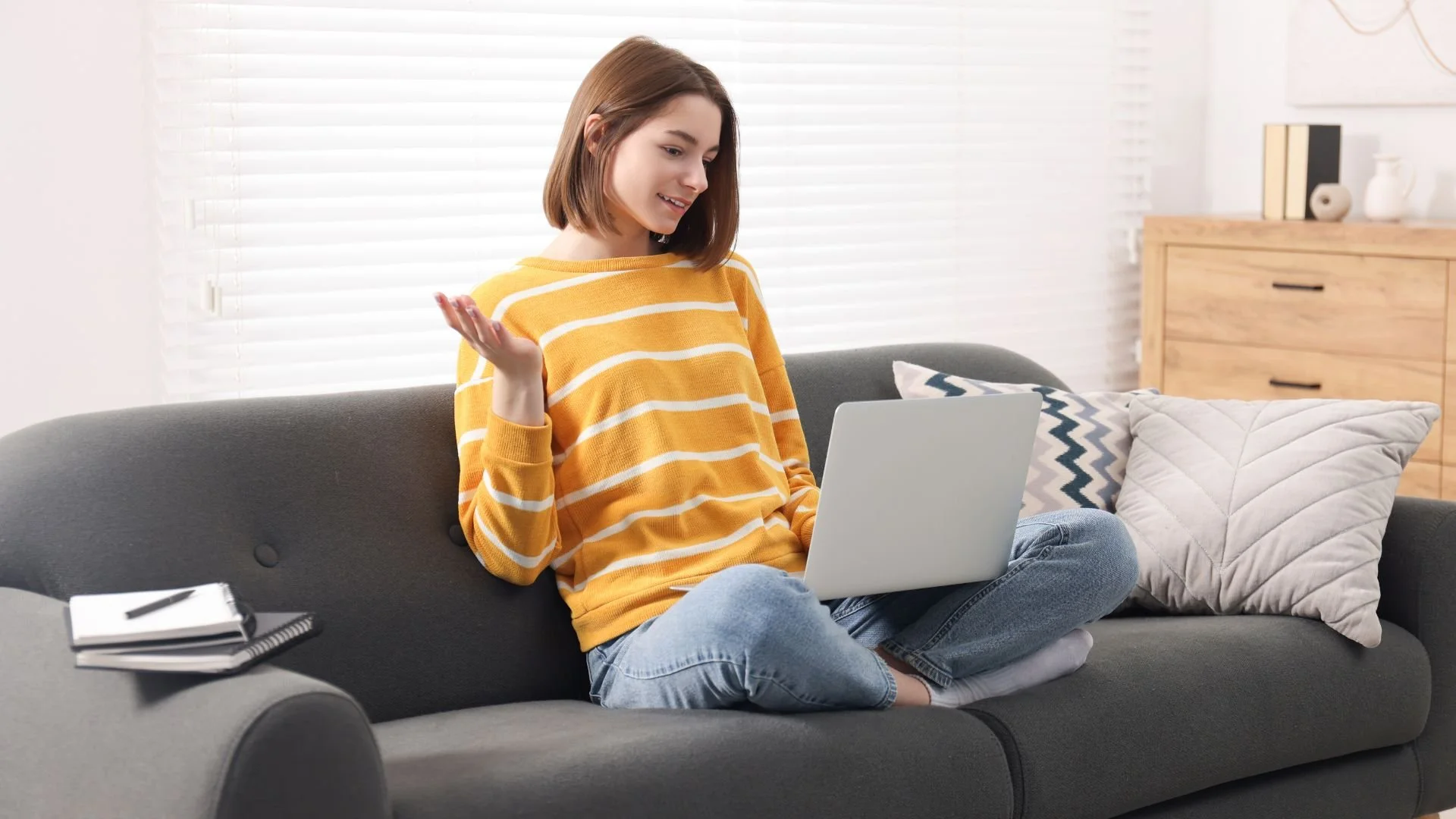 Young woman sitting on a gray couch participating in an online therapy session on her laptop.
