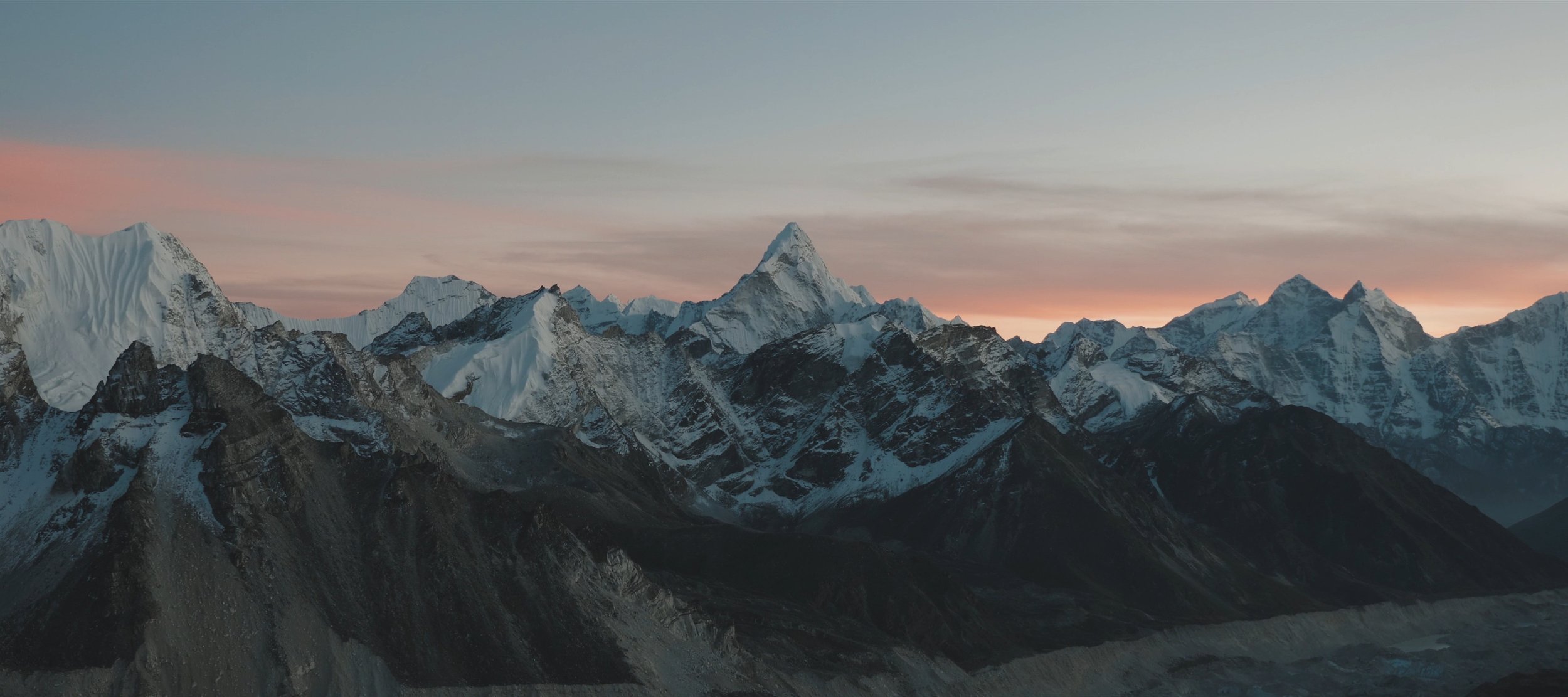 Snow-capped mountain range at sunset with a pink and blue sky.