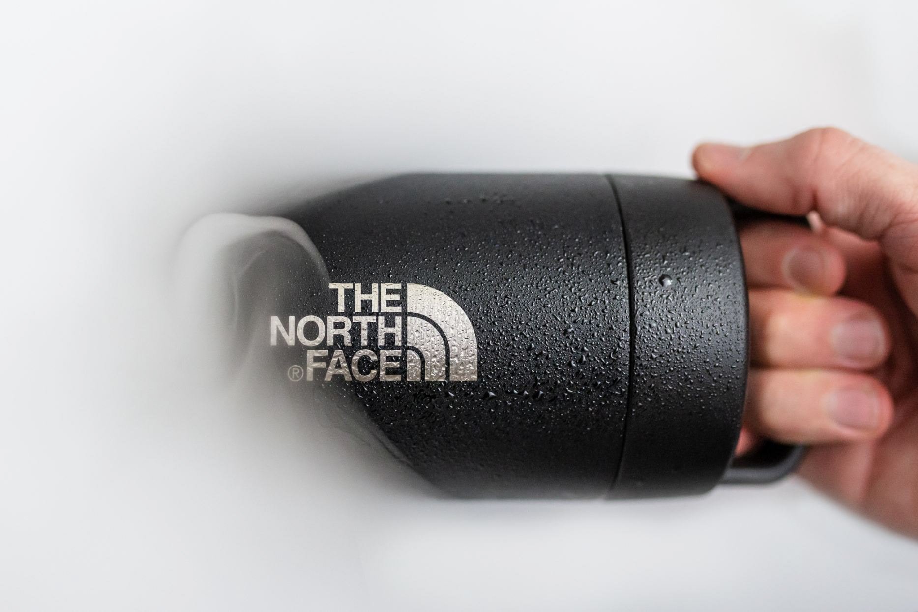 A hand holding a black thermos with water droplets and The North Face logo