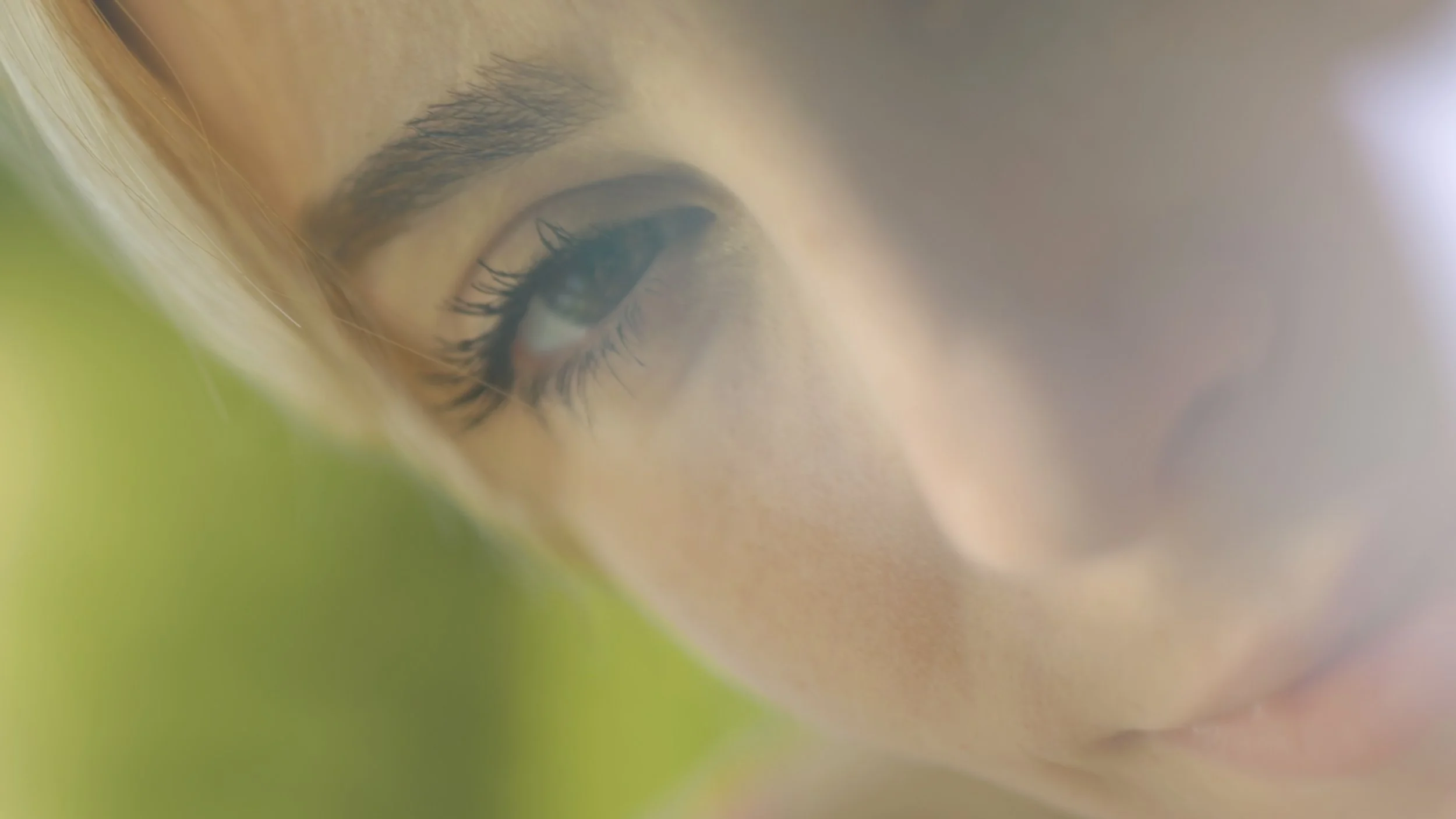 Close-up of a woman's face showing her eye, eyebrow, and part of her nose and lips with soft lighting and gentle focus.