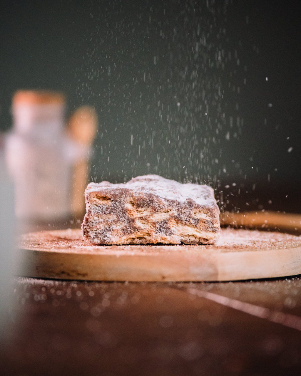 A piece of dough is being dusted with flour on a wooden surface, with flour particles falling in the air.