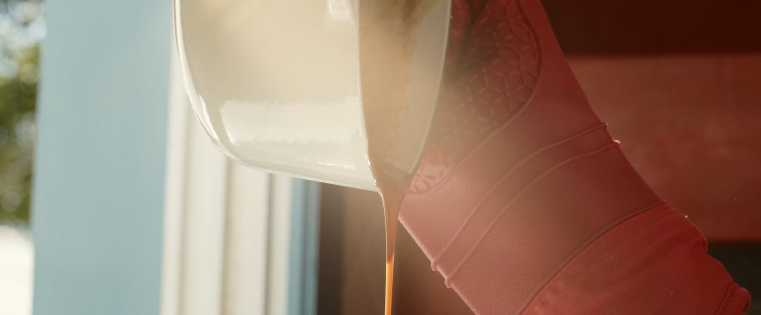 A glass of milk with chocolate syrup being poured into it, on a pink textured armrest or cushion.