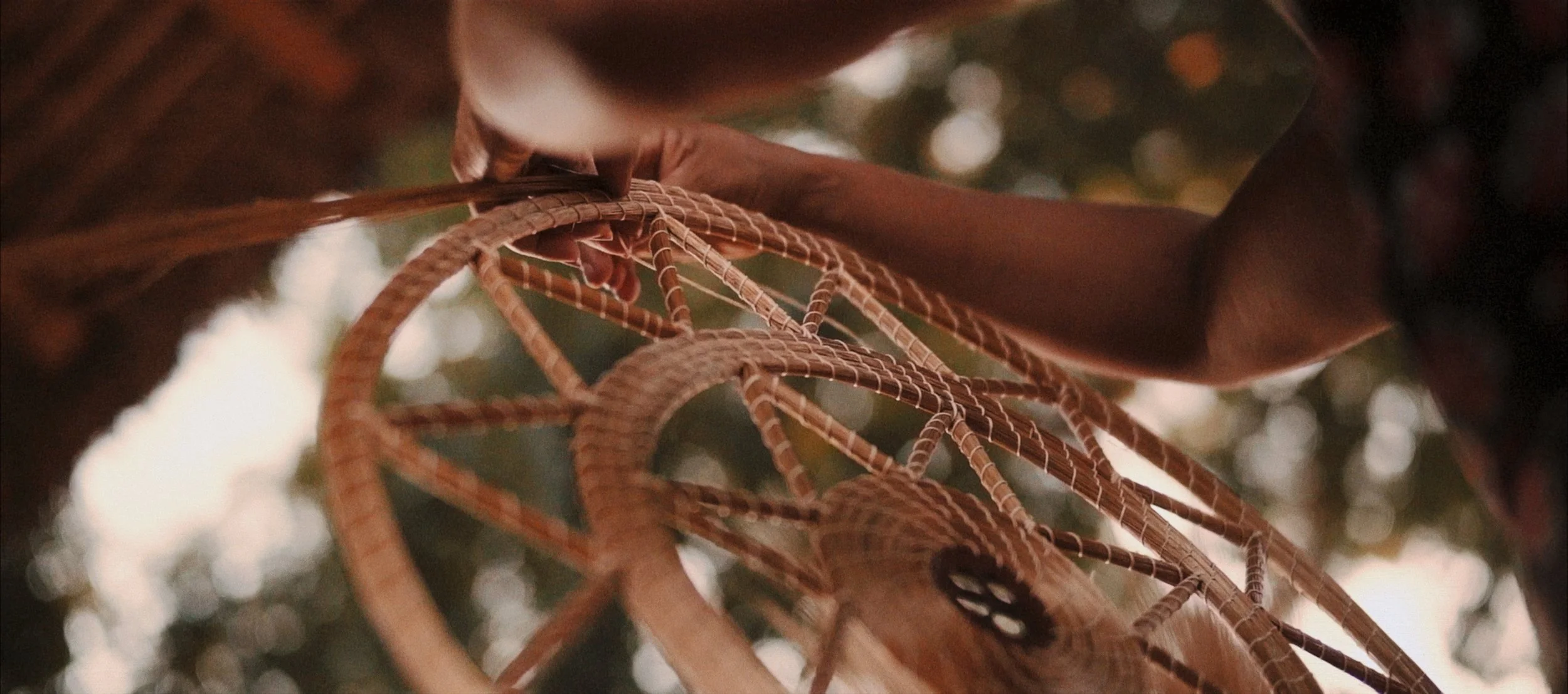 Close-up of a person's hand holding a handcrafted dreamcatcher with intricate woven details, outdoors with blurred background.