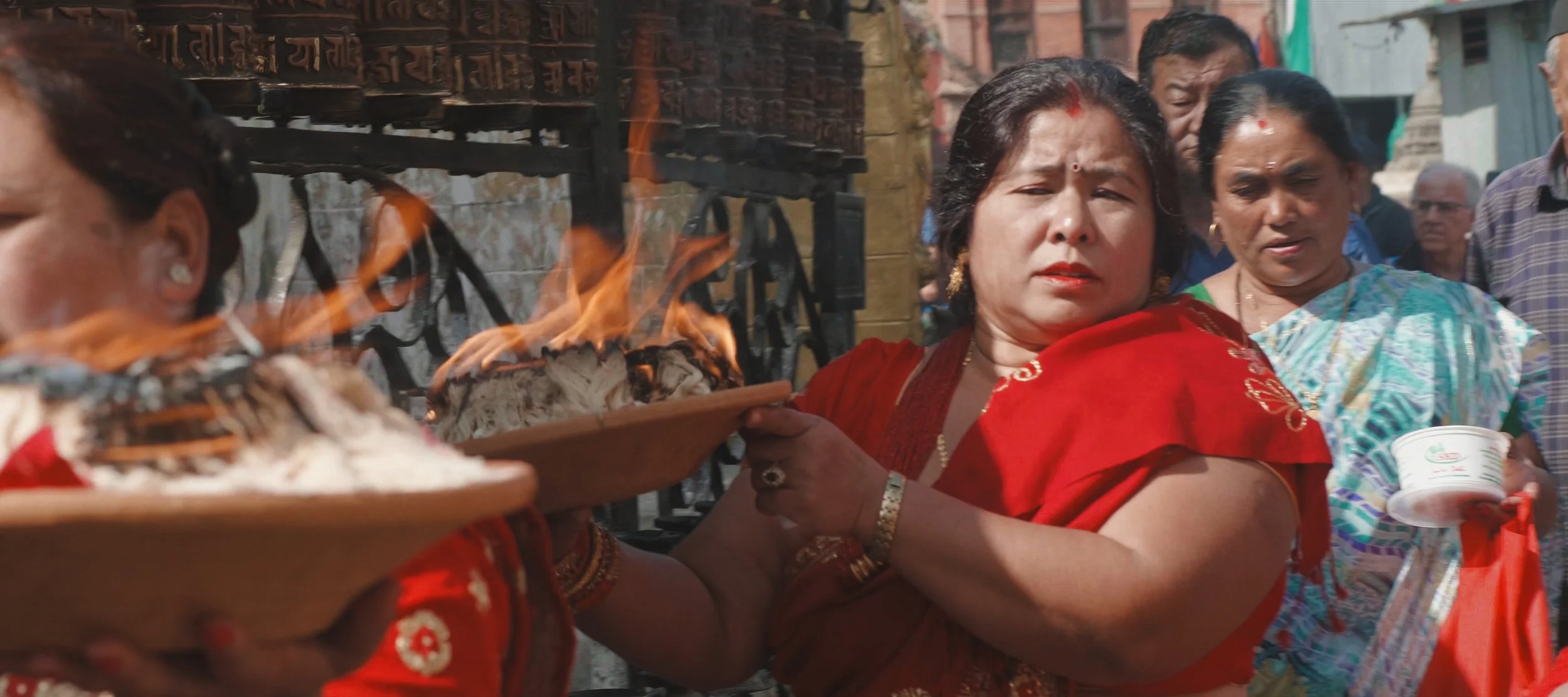 Group of women participating in a traditional ceremony, some holding plates with fire and offerings, wearing colorful traditional clothing.