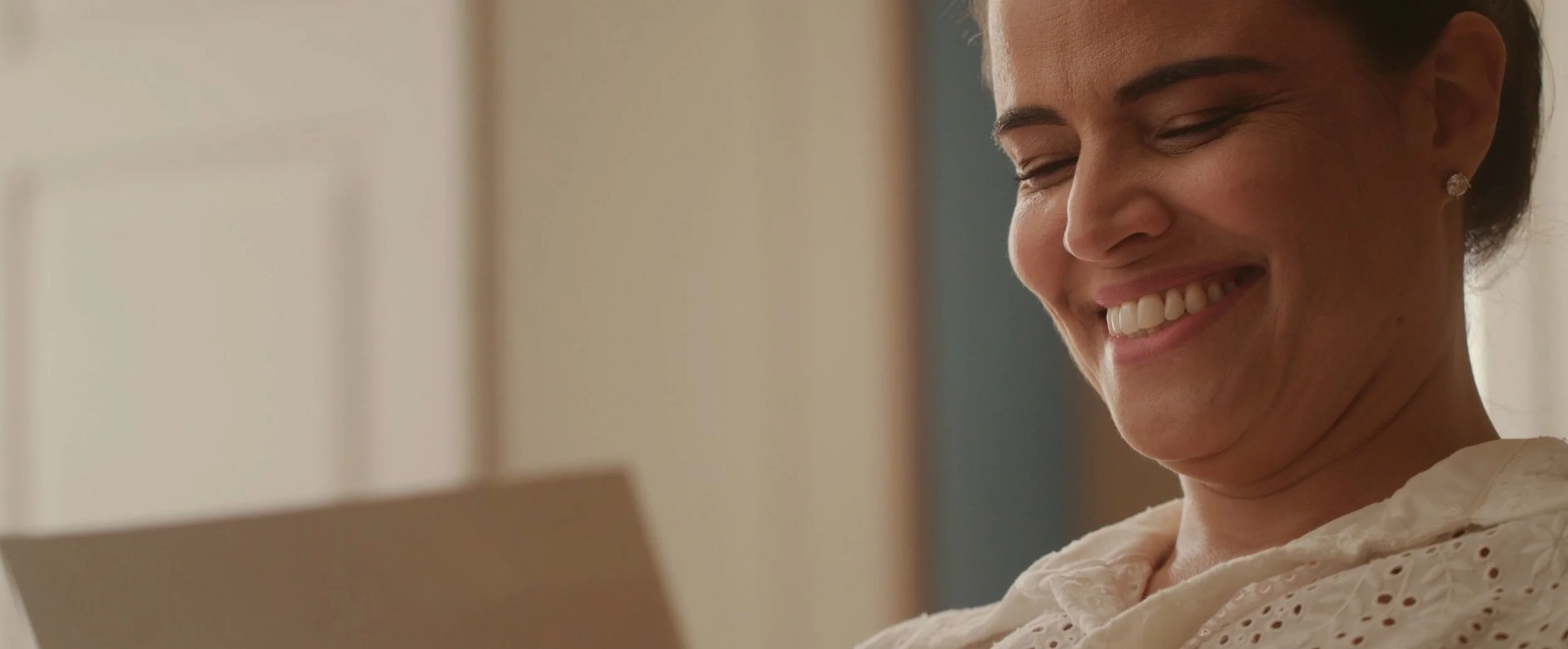 A woman smiling and looking at a tablet or book.