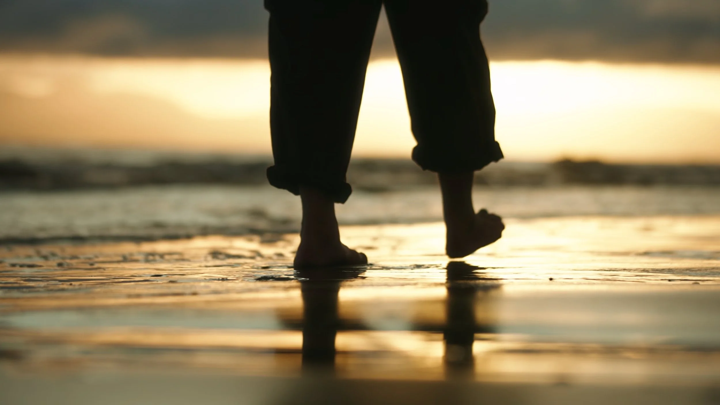 Person walking barefoot on the beach during sunset