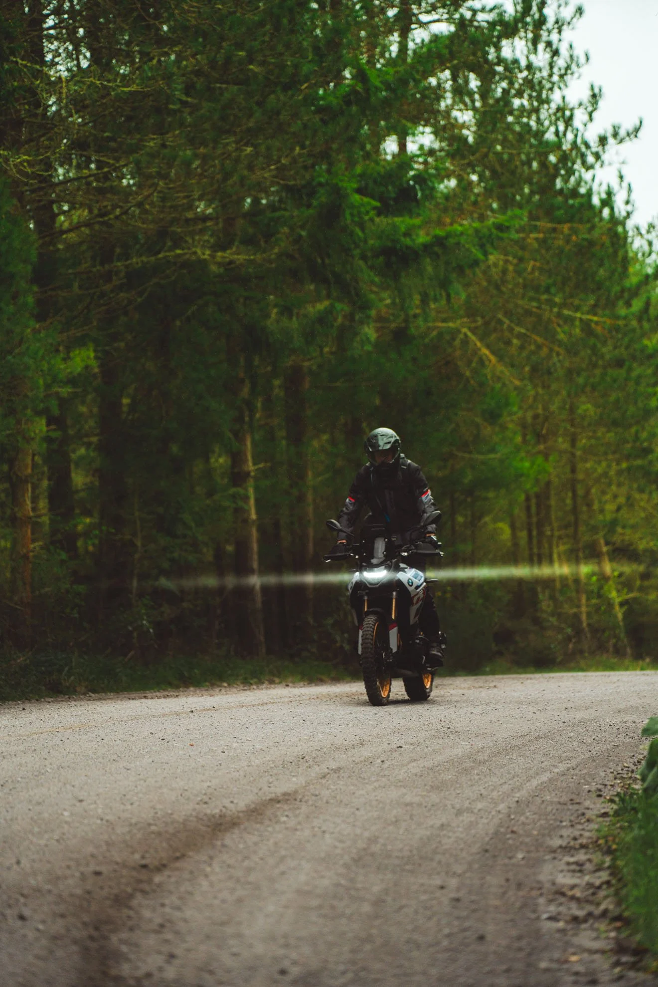 A person riding an off-road motorcycle on a gravel forest trail during daytime.
