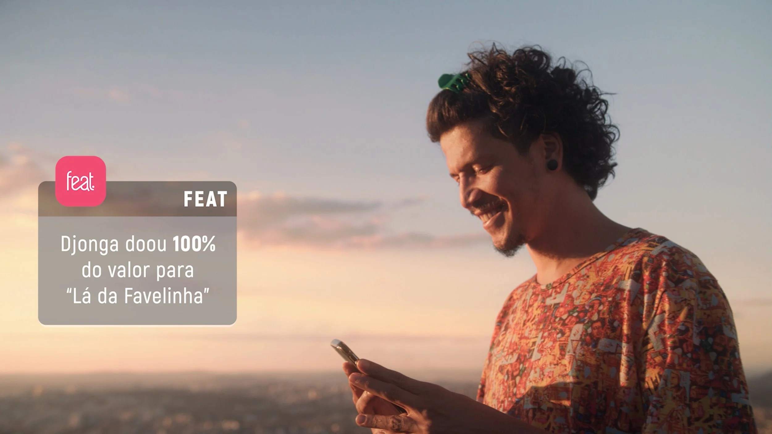 A man with curly hair and a colorful shirt looking at his phone outdoors during sunset.
