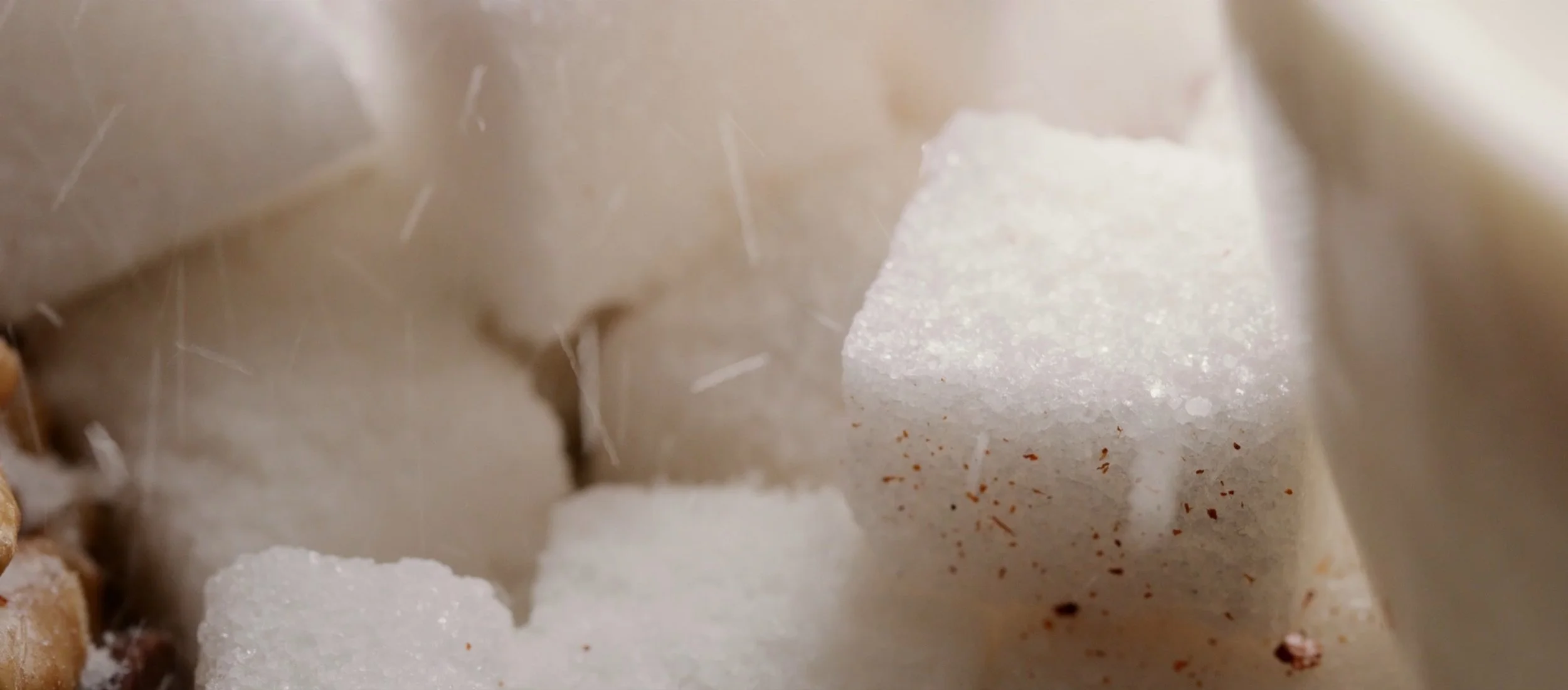 Close-up image of white sugar cubes with brown specks, surrounded by sugar crystals and granules.