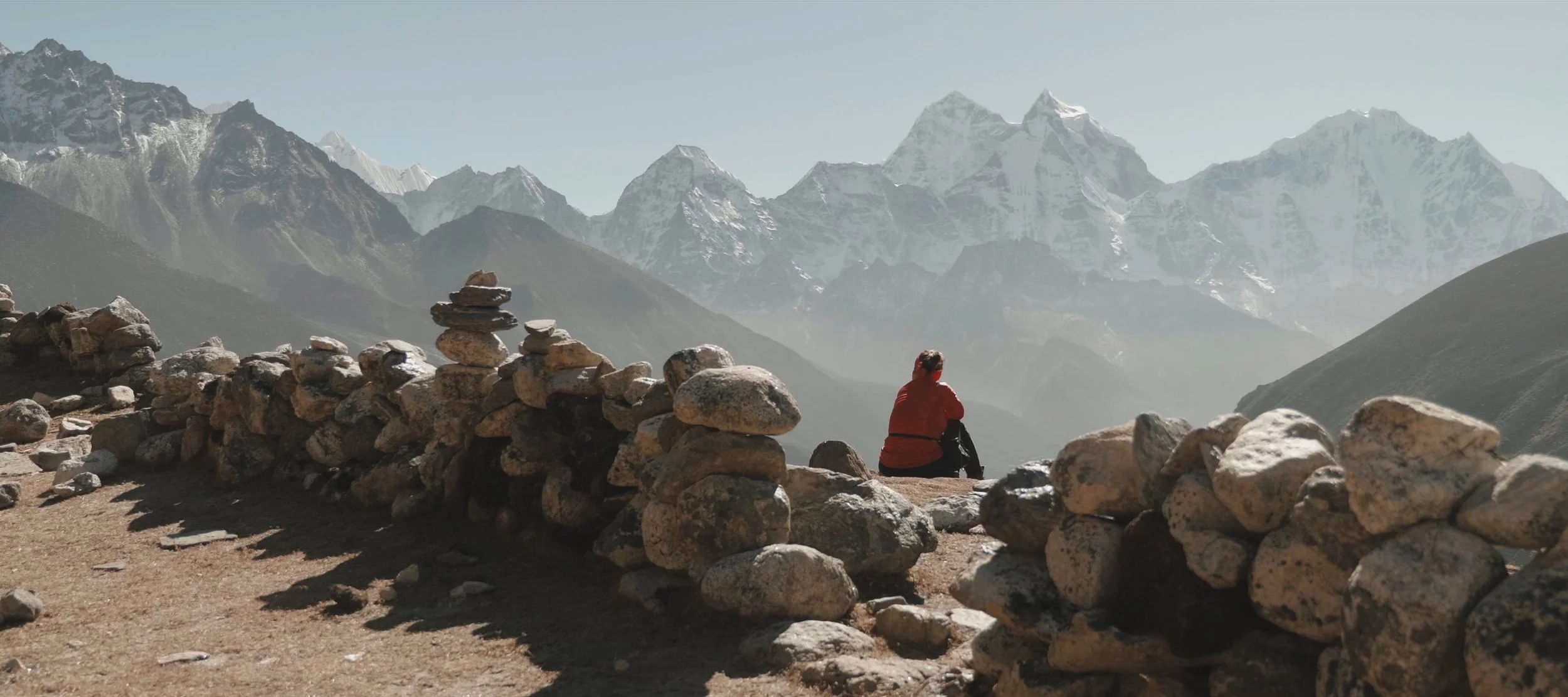 A person sitting on rocks and looking at snow-capped mountains in the distance.