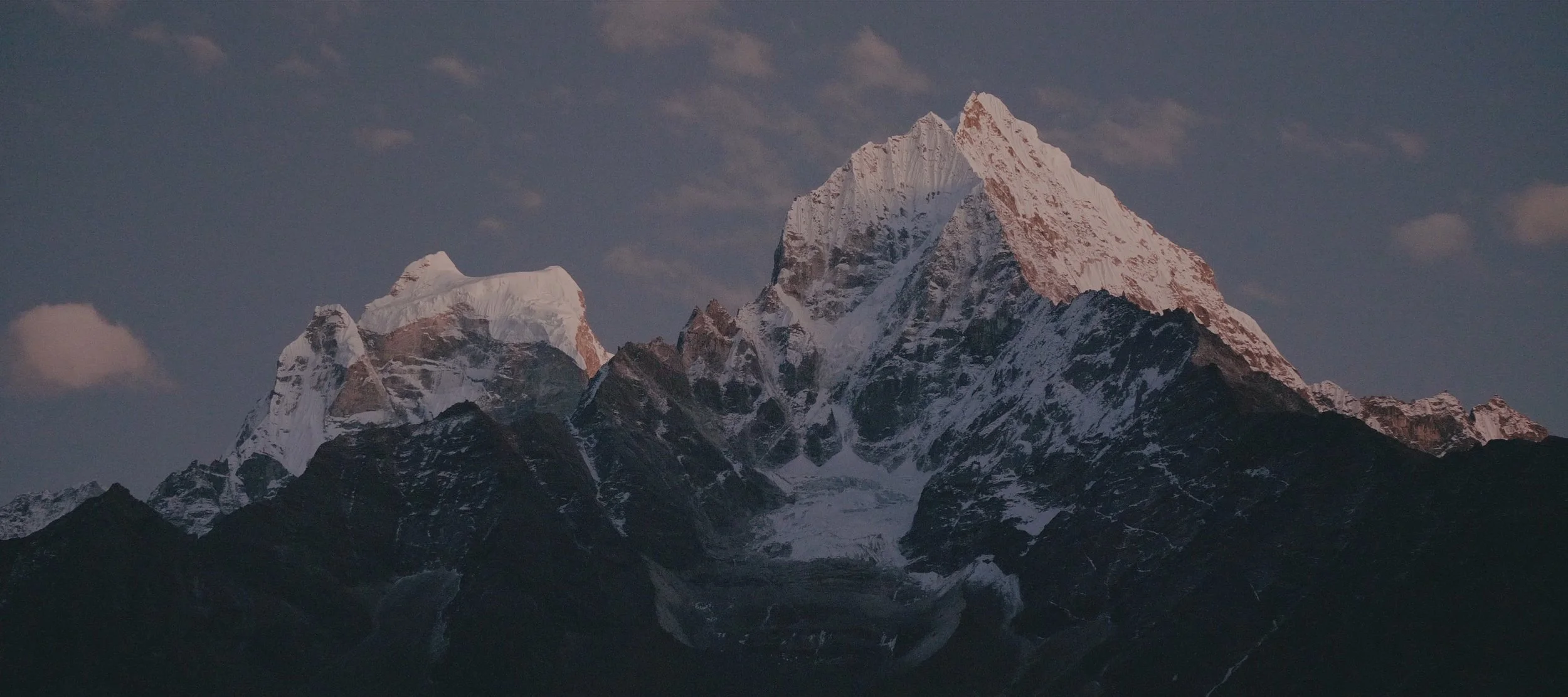 A tall mountain covered in snow against a partly cloudy sky.