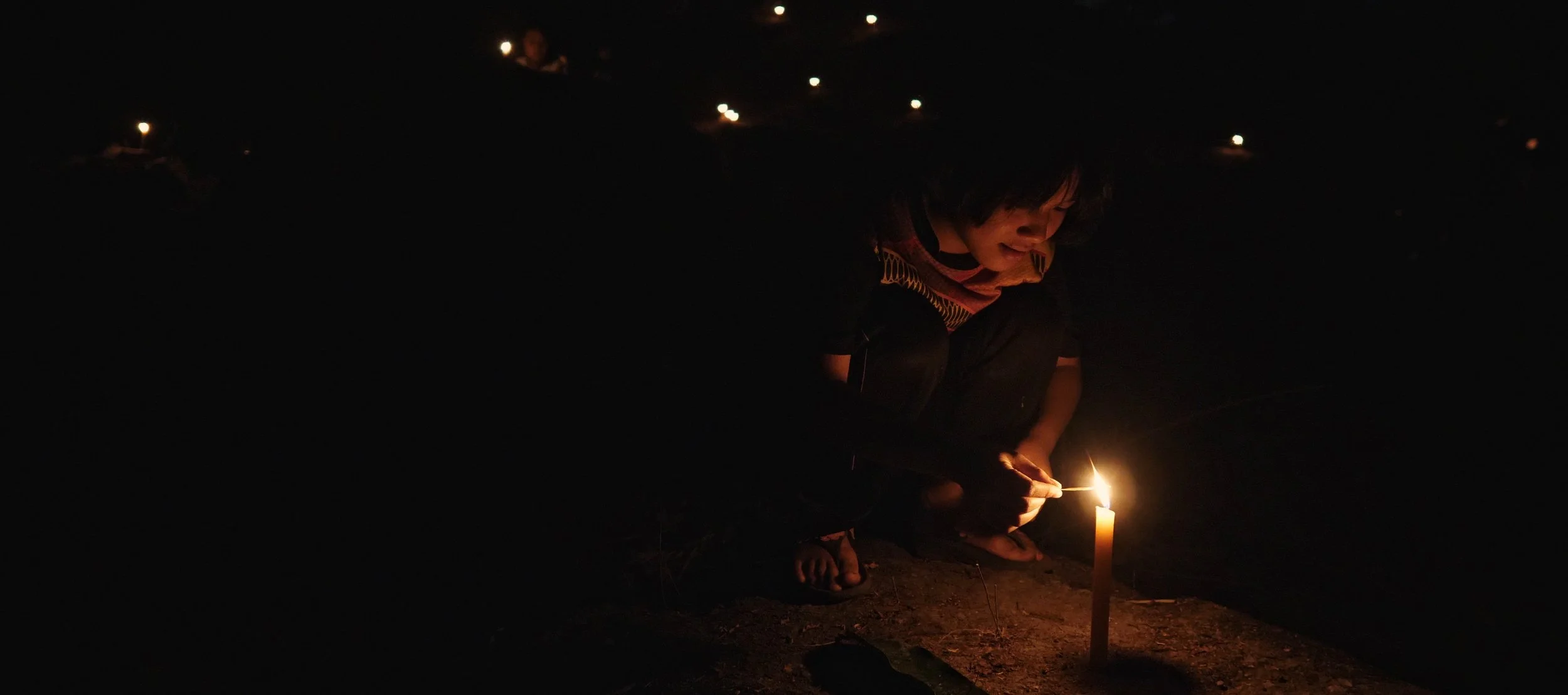 Person lighting a candle in the dark.