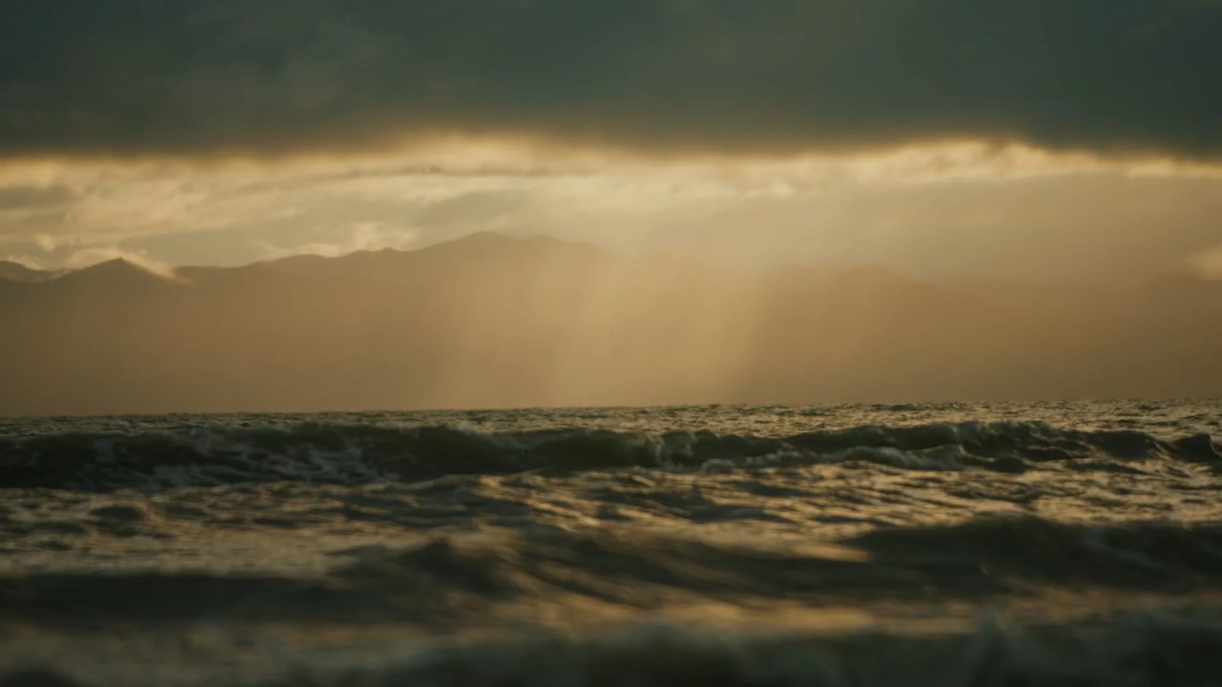 A photo of ocean waves under a cloudy sky with rays of sunlight coming through, creating a dramatic and serene scene.