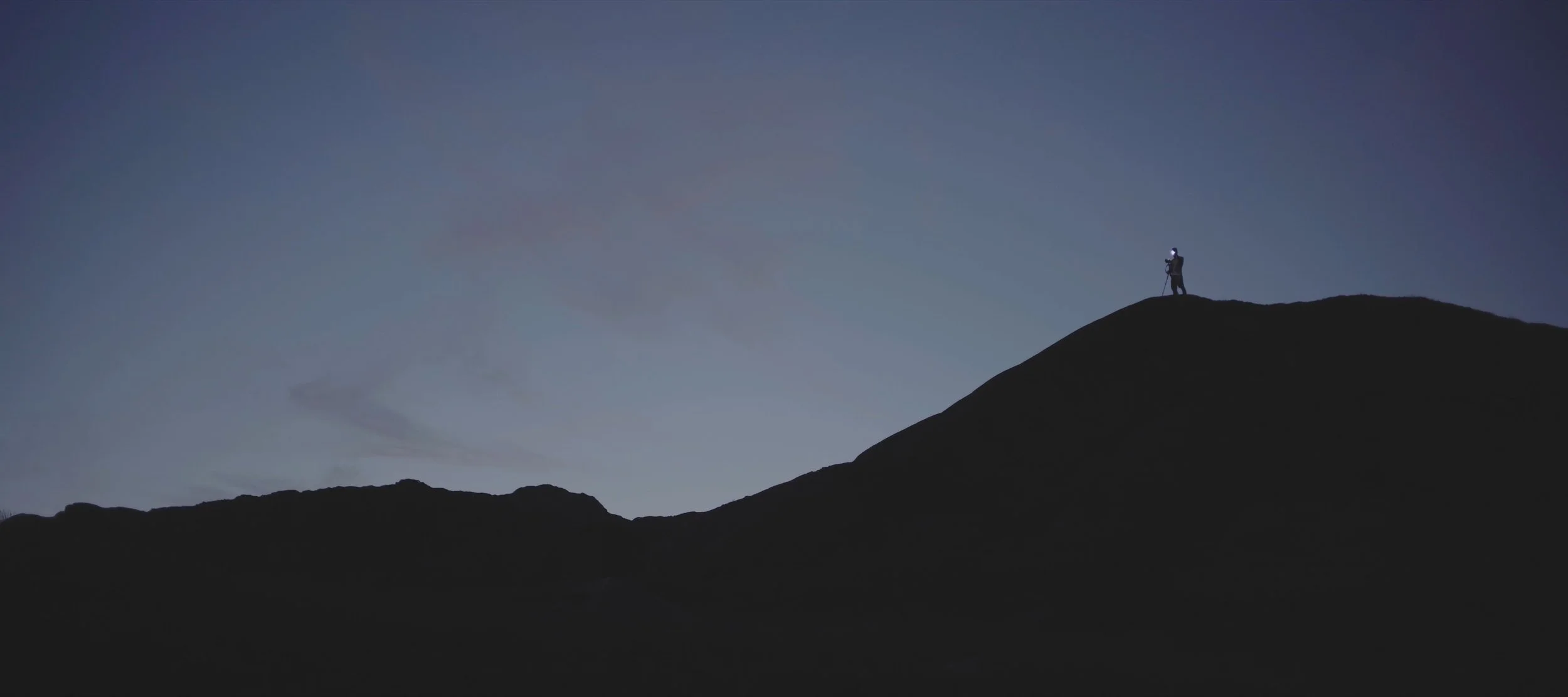 Silhouette of a hiker on a mountain at dusk with a clear sky.