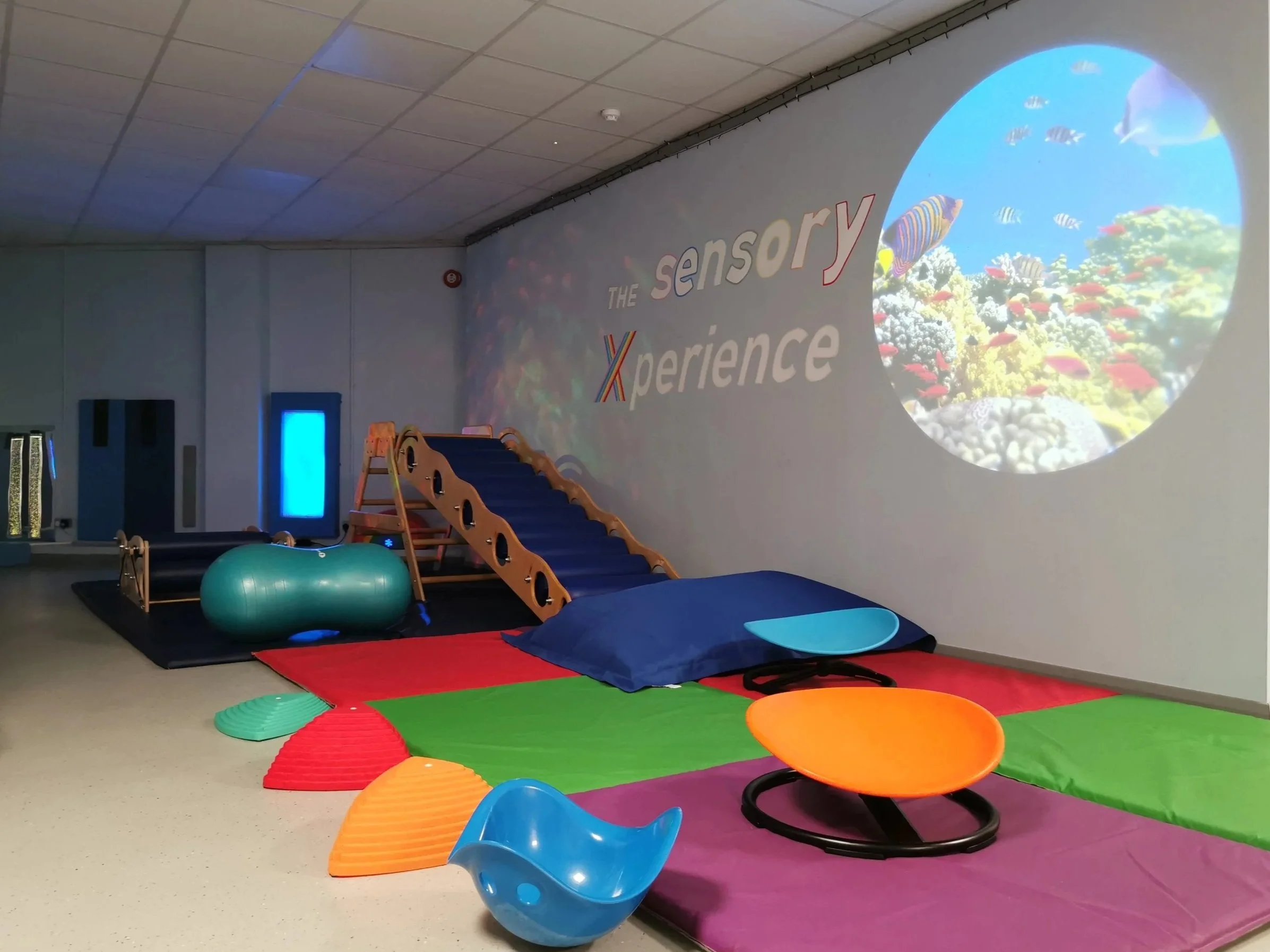 Indoor sensory play area with foam mats, balance equipment, and a projected underwater scene on the wall.