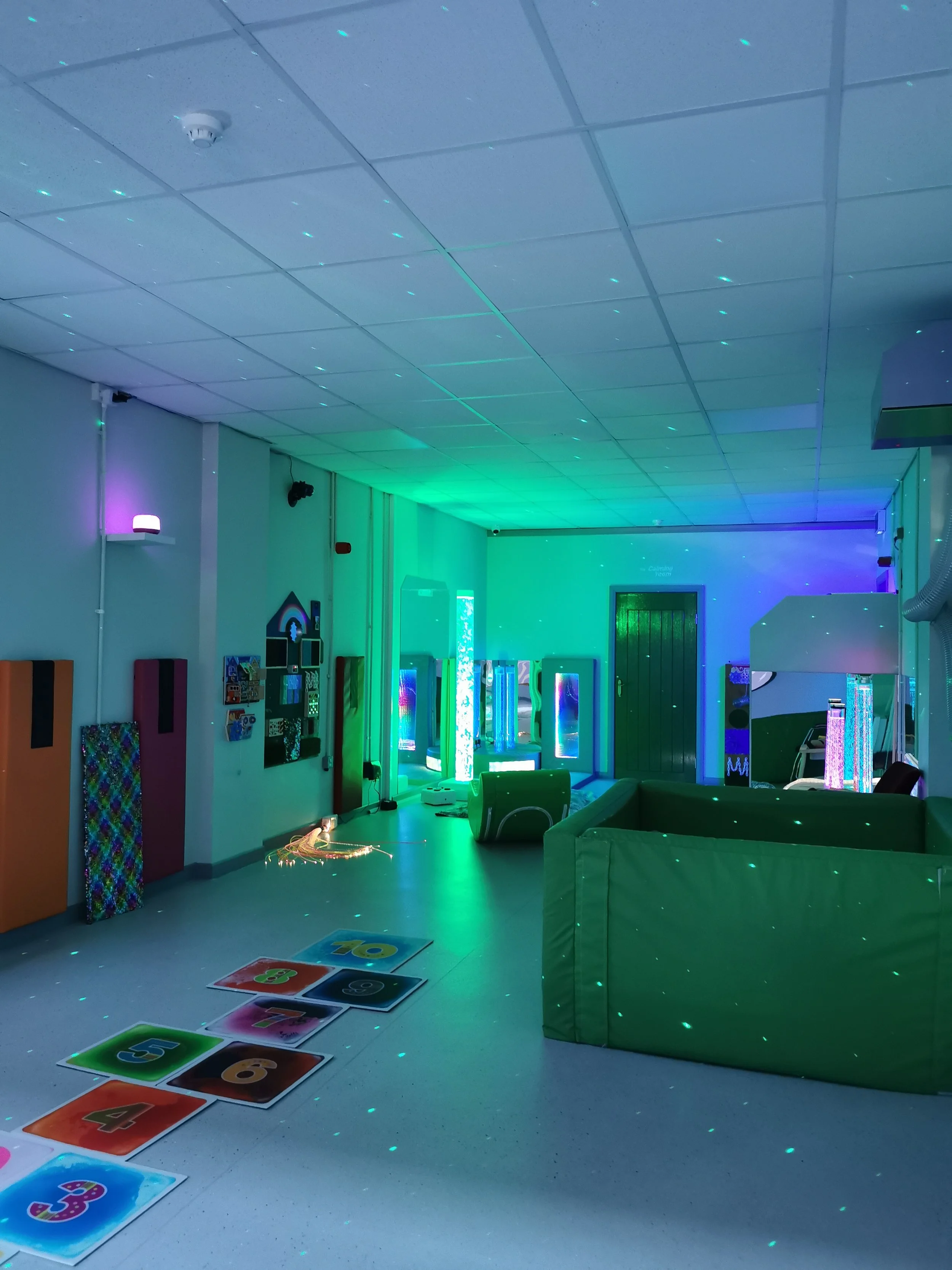 Multi-sensory room with colourful relaxing lights, a ball pool and sensory hopscotch on the floor.