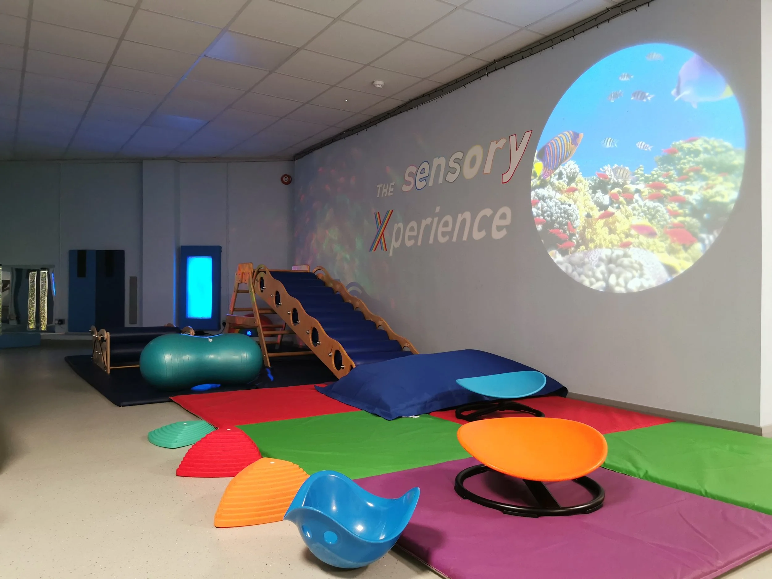 Indoor sensory play area with foam mats, balance equipment, and a projected underwater scene on the wall.
