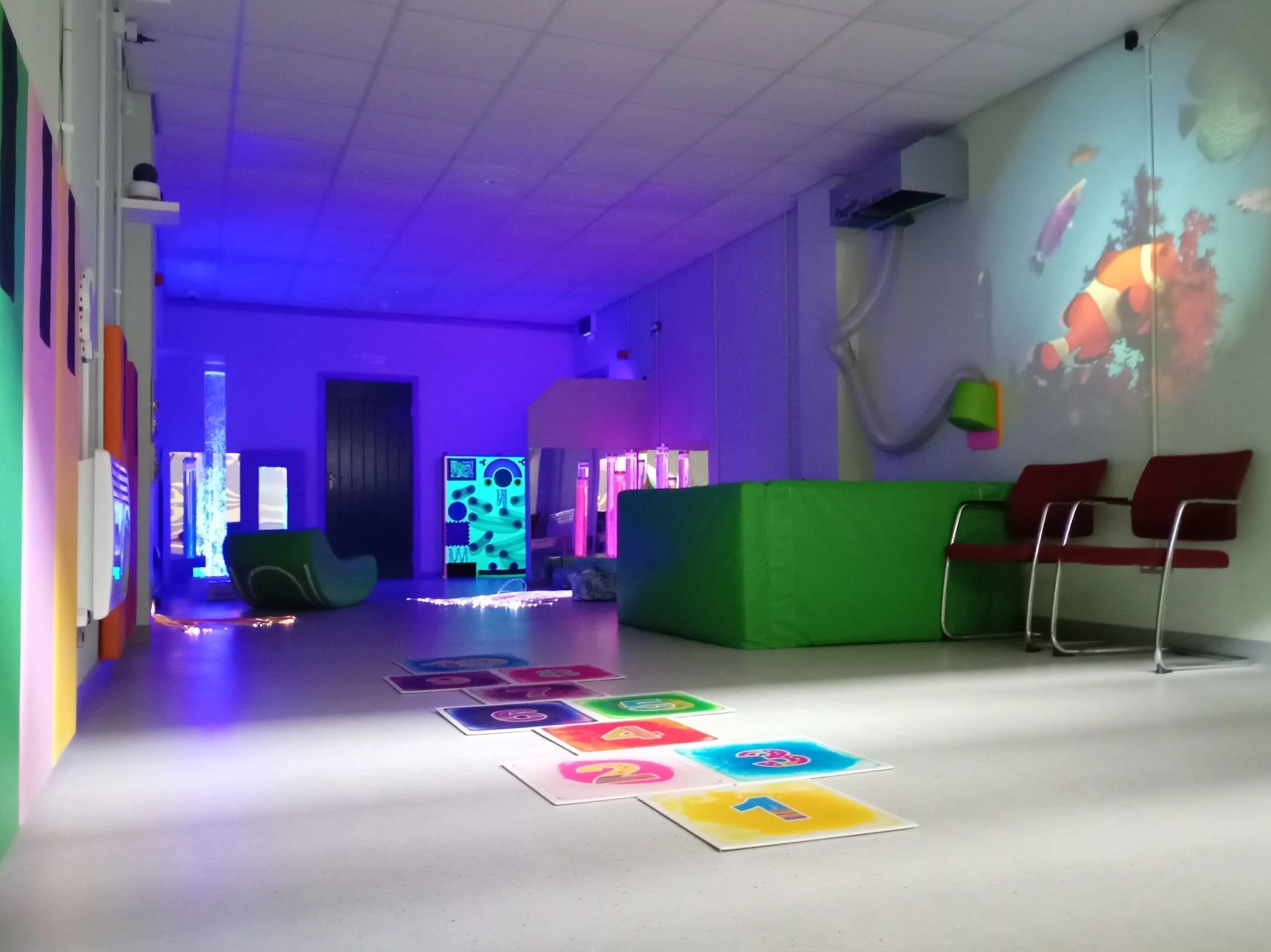 Multi-sensory room with colourful relaxing lights, a ball pool and sensory hopscotch on the floor.