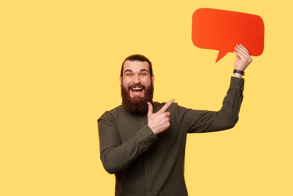 A bearded man cheerfuly pointing at a speech bubble while looking at the camera - Cristalov @ Deposit Photos 598069404