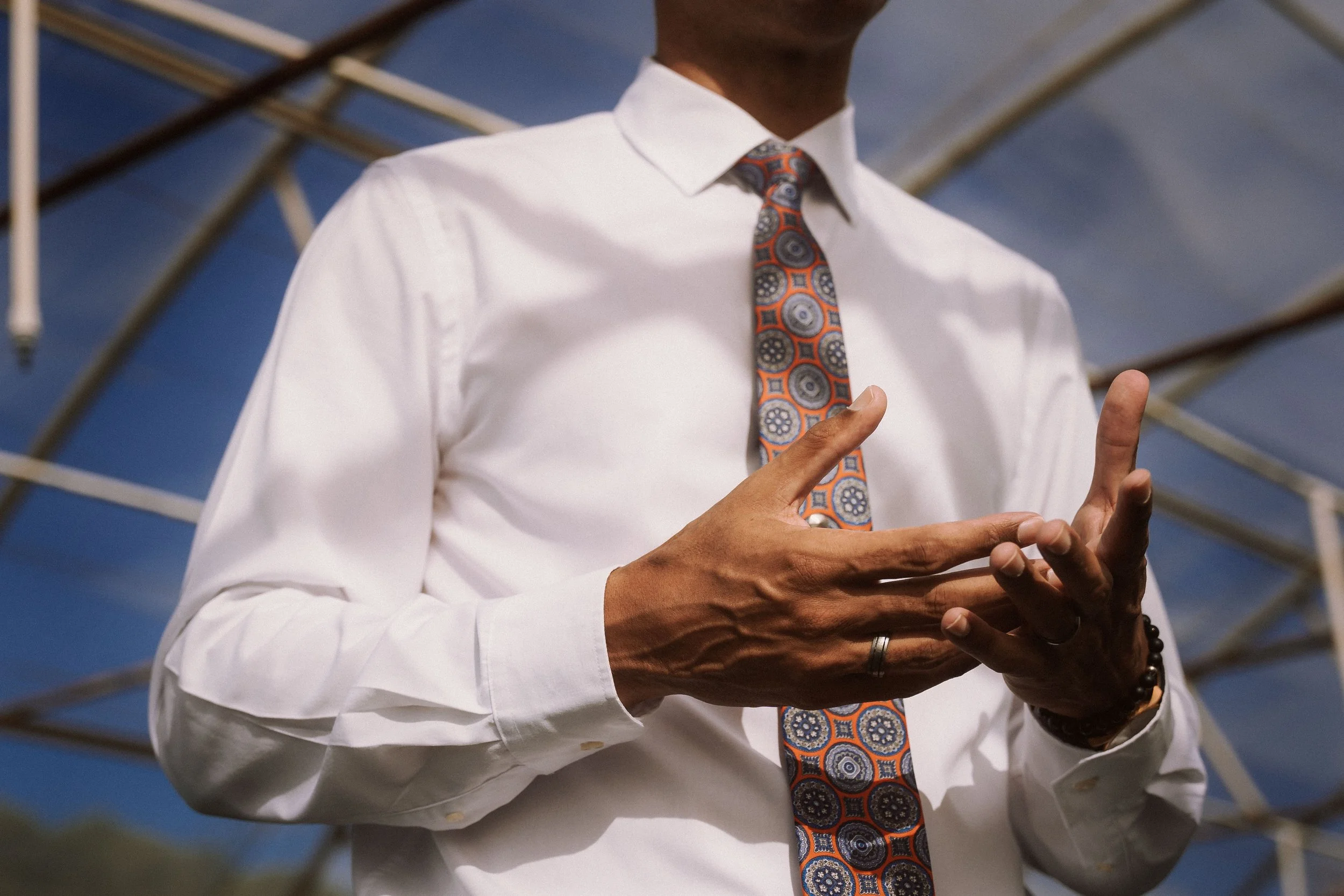 Close-up of a person wearing a white dress shirt and patterned tie, gesturing with hands.
