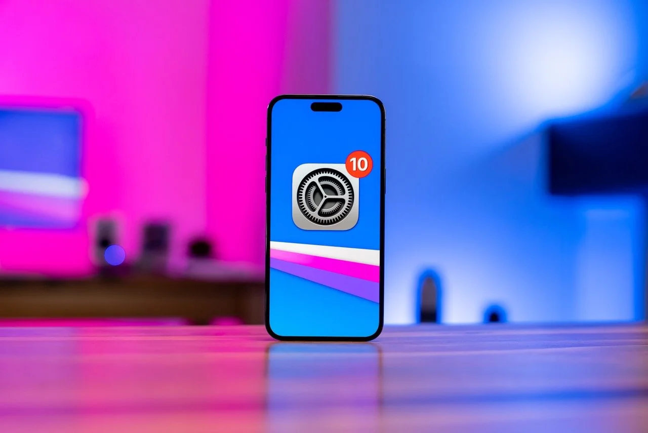 Uno smartphone con l'icona delle impostazioni e una notifica con il numero 10 sullo schermo, posizionato su un tavolo con sfondo a luci colorate.
