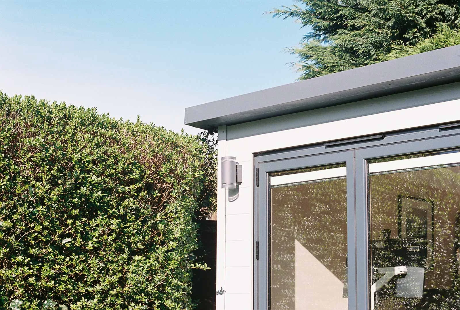 Contemporary garden room with large glass bi-fold doors, surrounded by greenery and hedging