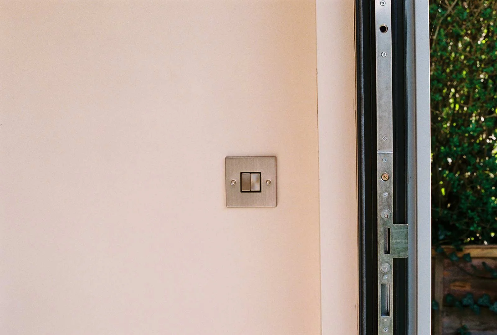 Close-up of a minimalist wall with a brushed metal light switch beside a doorway inside a garden room