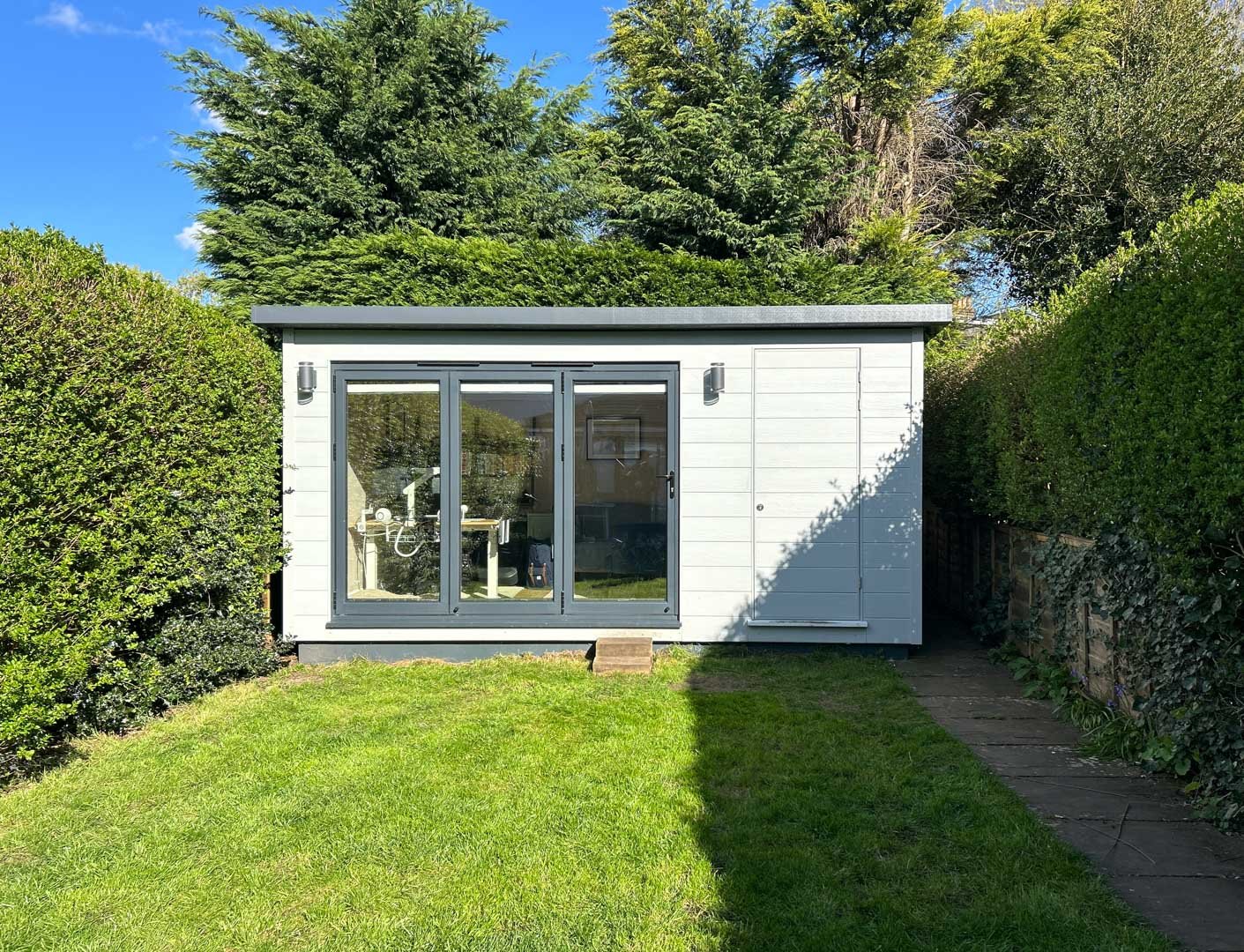 Bespoke garden room with flat roof, bi-fold doors and white composite exterior in a sunny garden