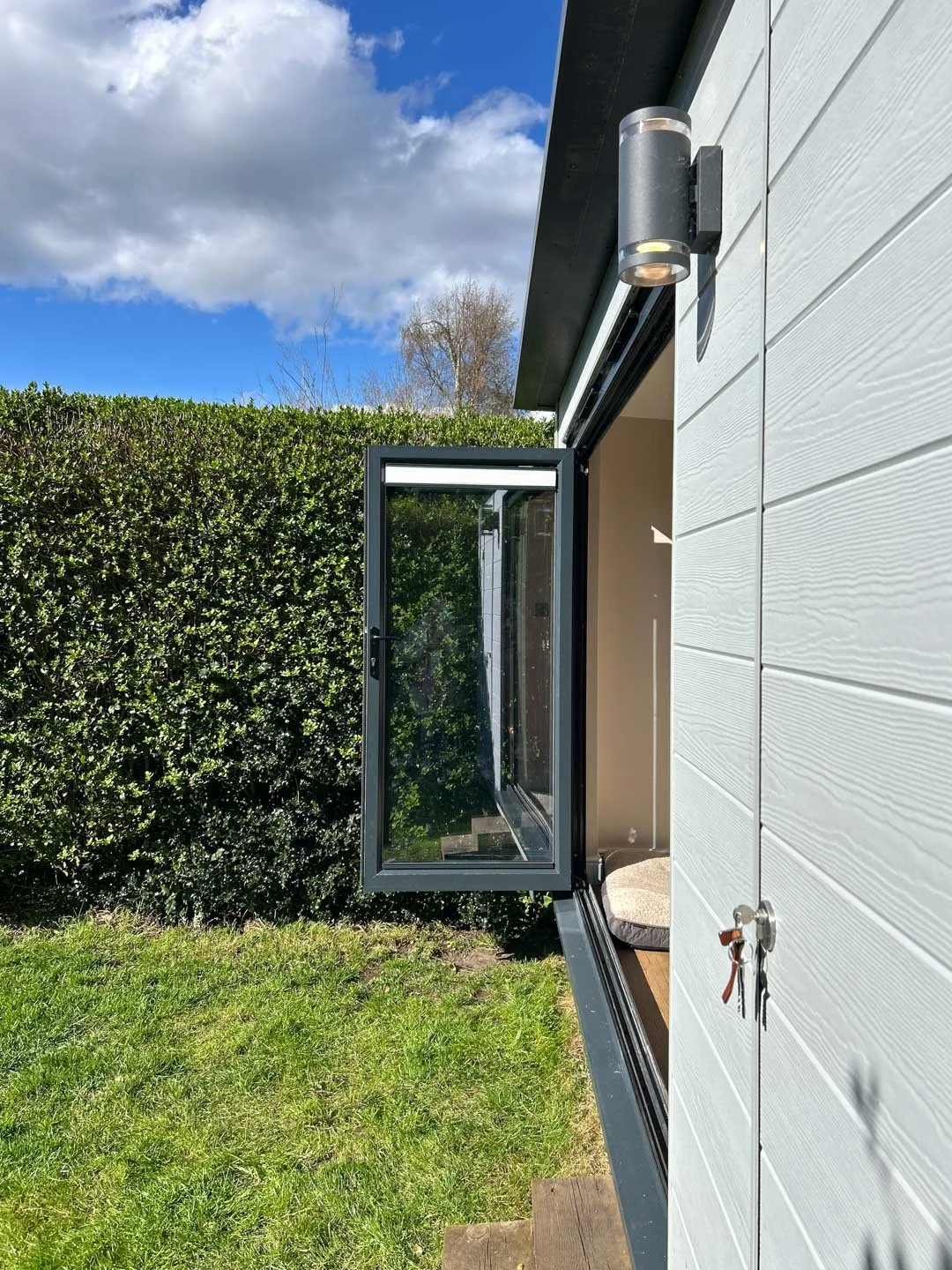 Side angle of garden room showing open window, composite cladding texture and garden surroundings
